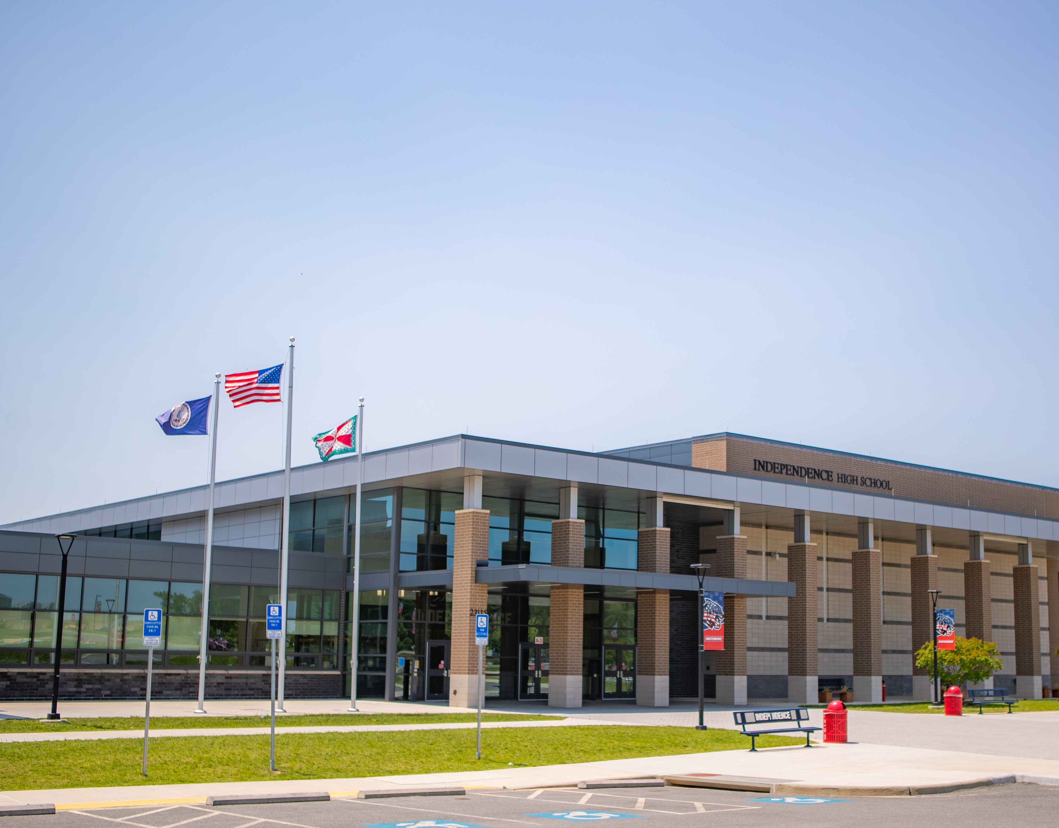A modern, multi-story building with glass walls and an American flag flying outside, surrounded by a grassy area and a paved walkway.
