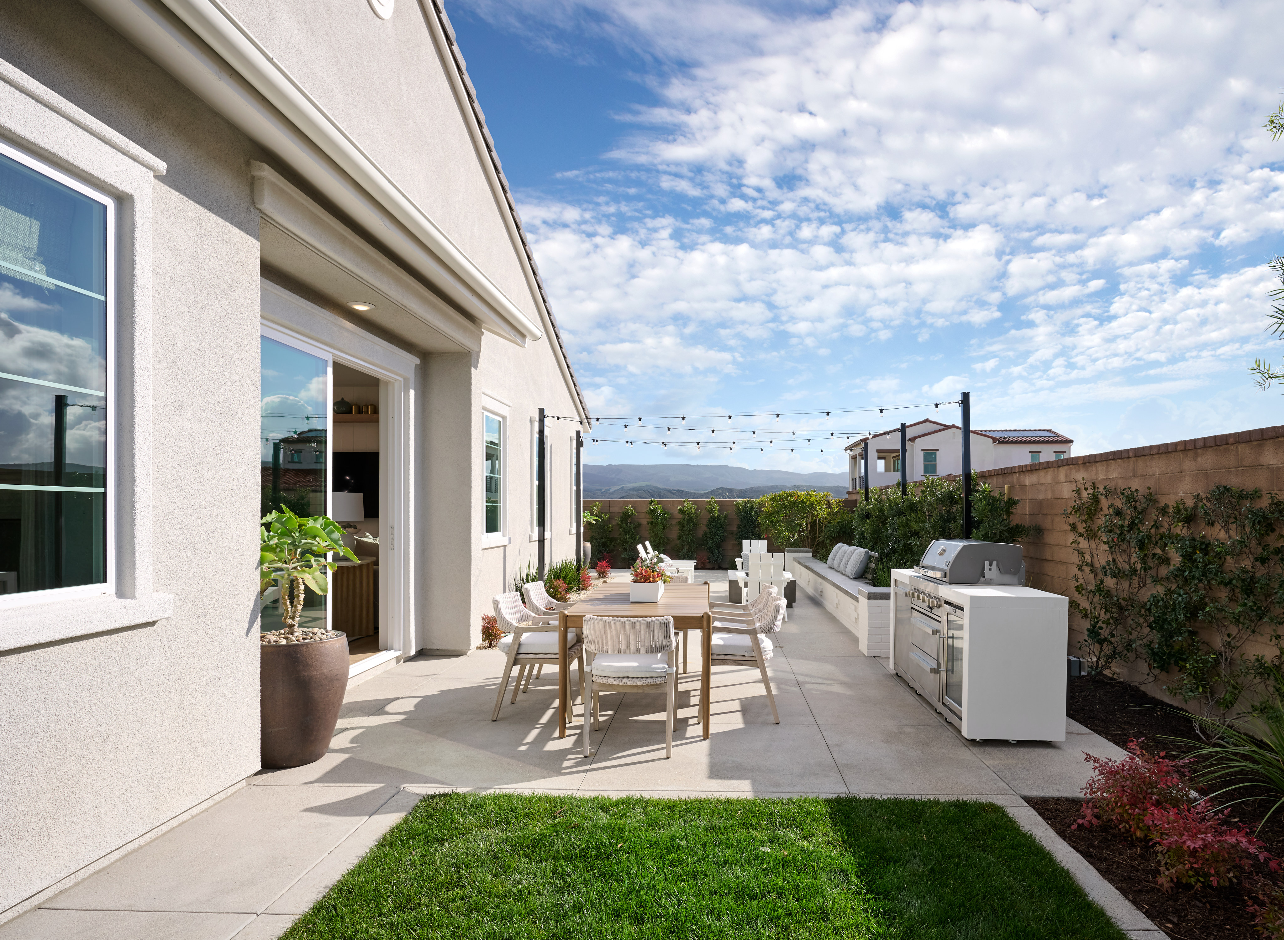A well-designed outdoor living space with a patio, dining area, and landscaping, set against a backdrop of a clear blue sky with fluffy clouds.