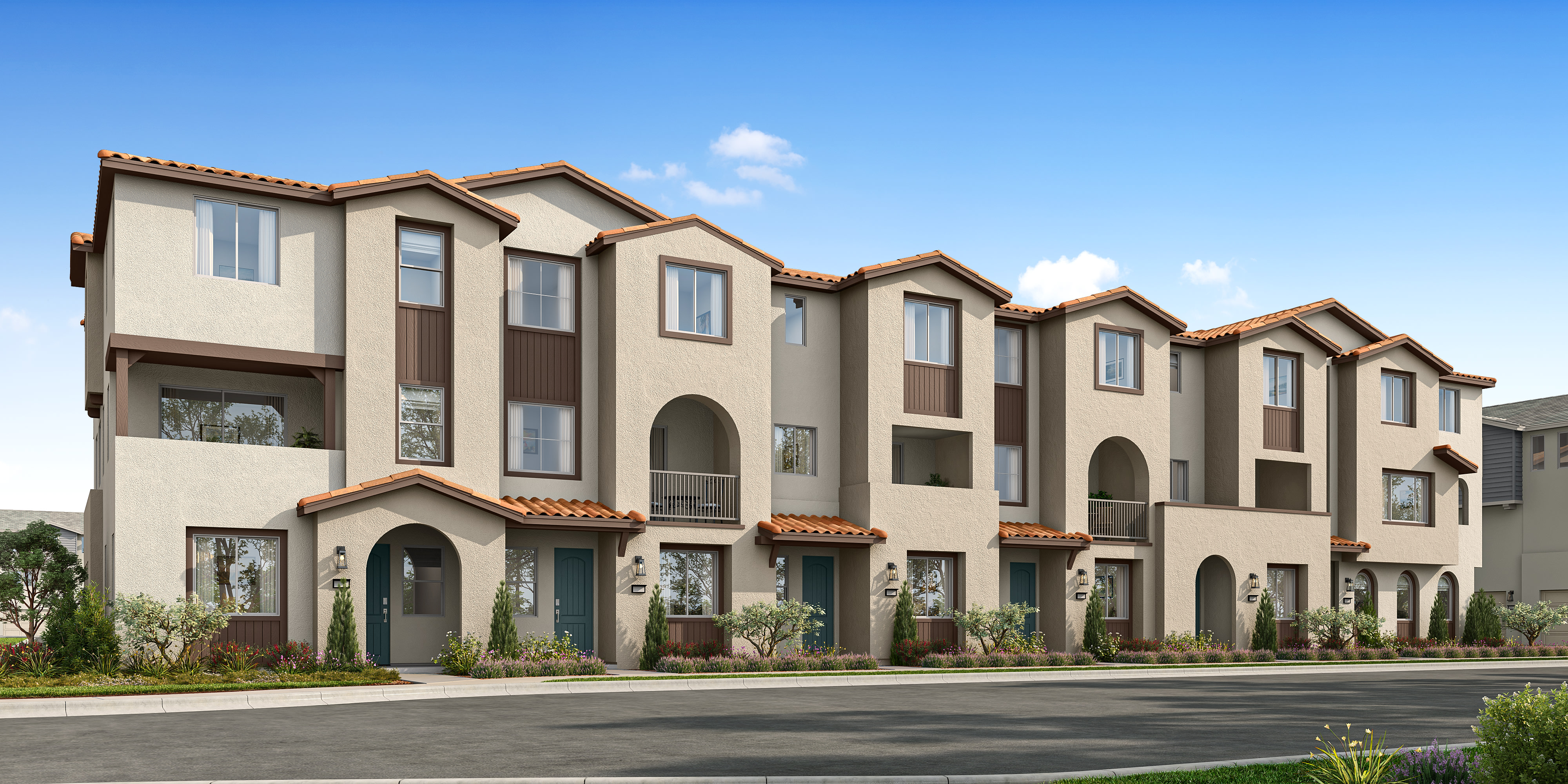 A row of multi-story townhouses with a mix of beige and brown exterior colors, set against a clear blue sky in the background.
