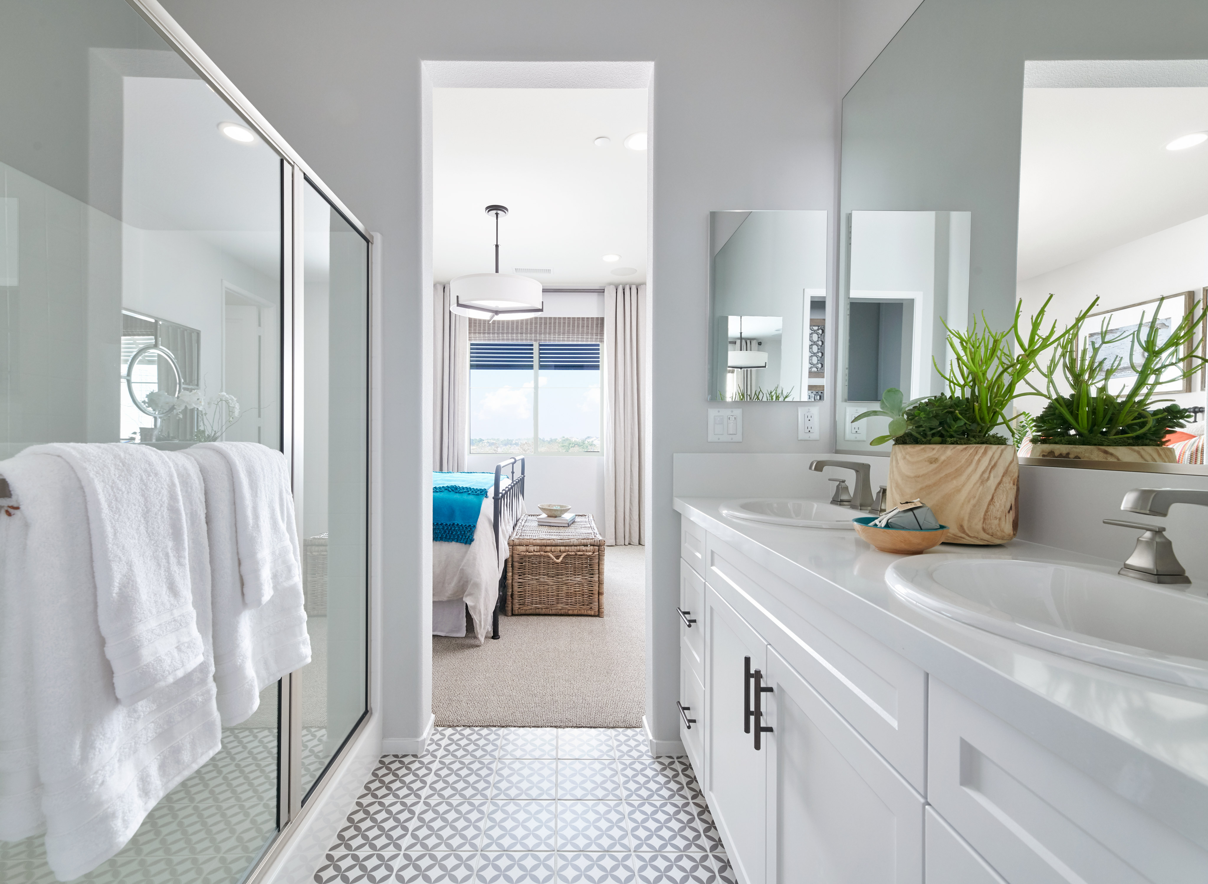 A bright and airy bathroom with white cabinets, a large mirror, and a potted plant, leading to an open doorway in the background.