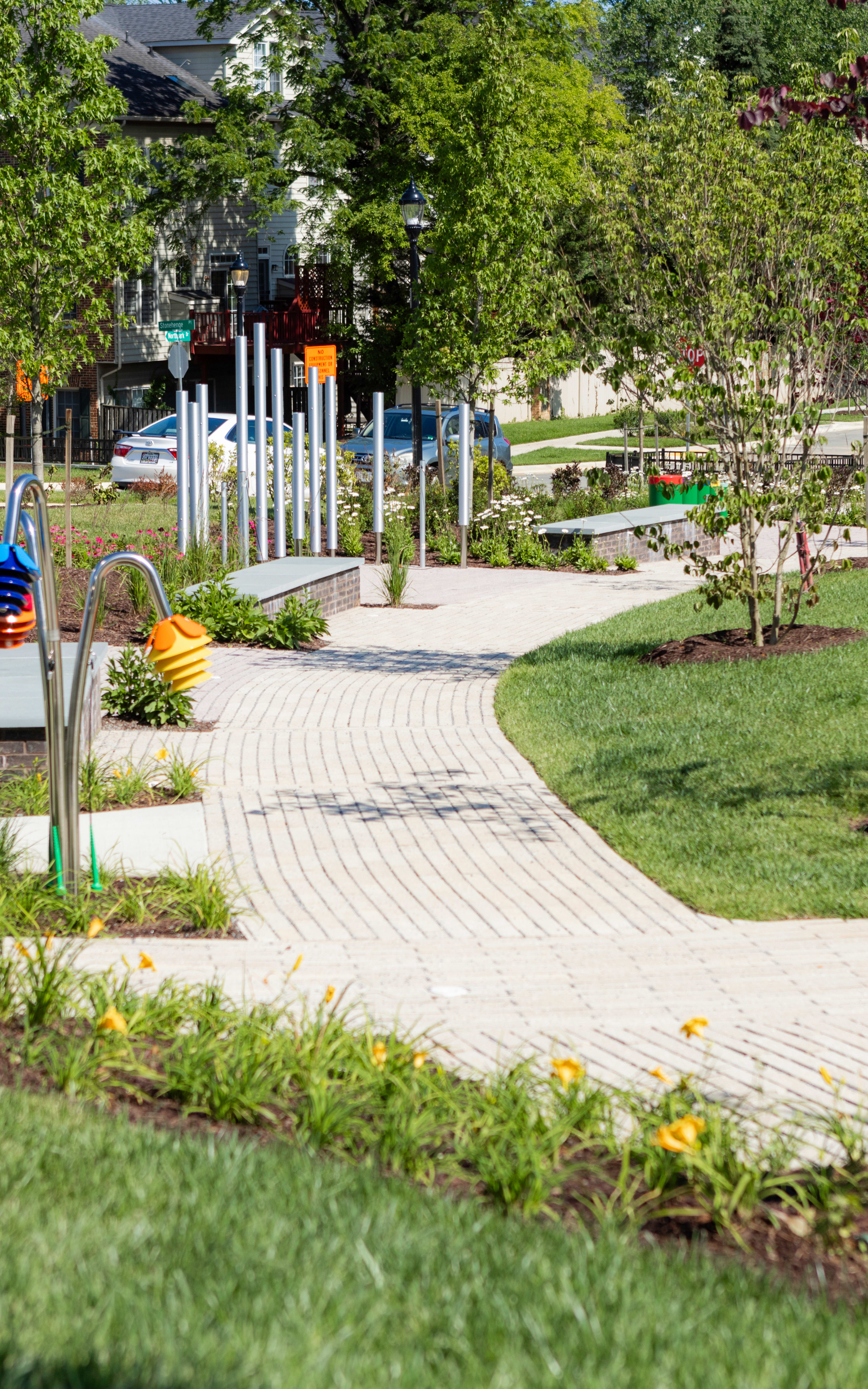 A well-maintained garden path winds through a lush, green landscape, with colorful sculptures and decorative elements lining the walkway, creating a vibrant and inviting outdoor space.
