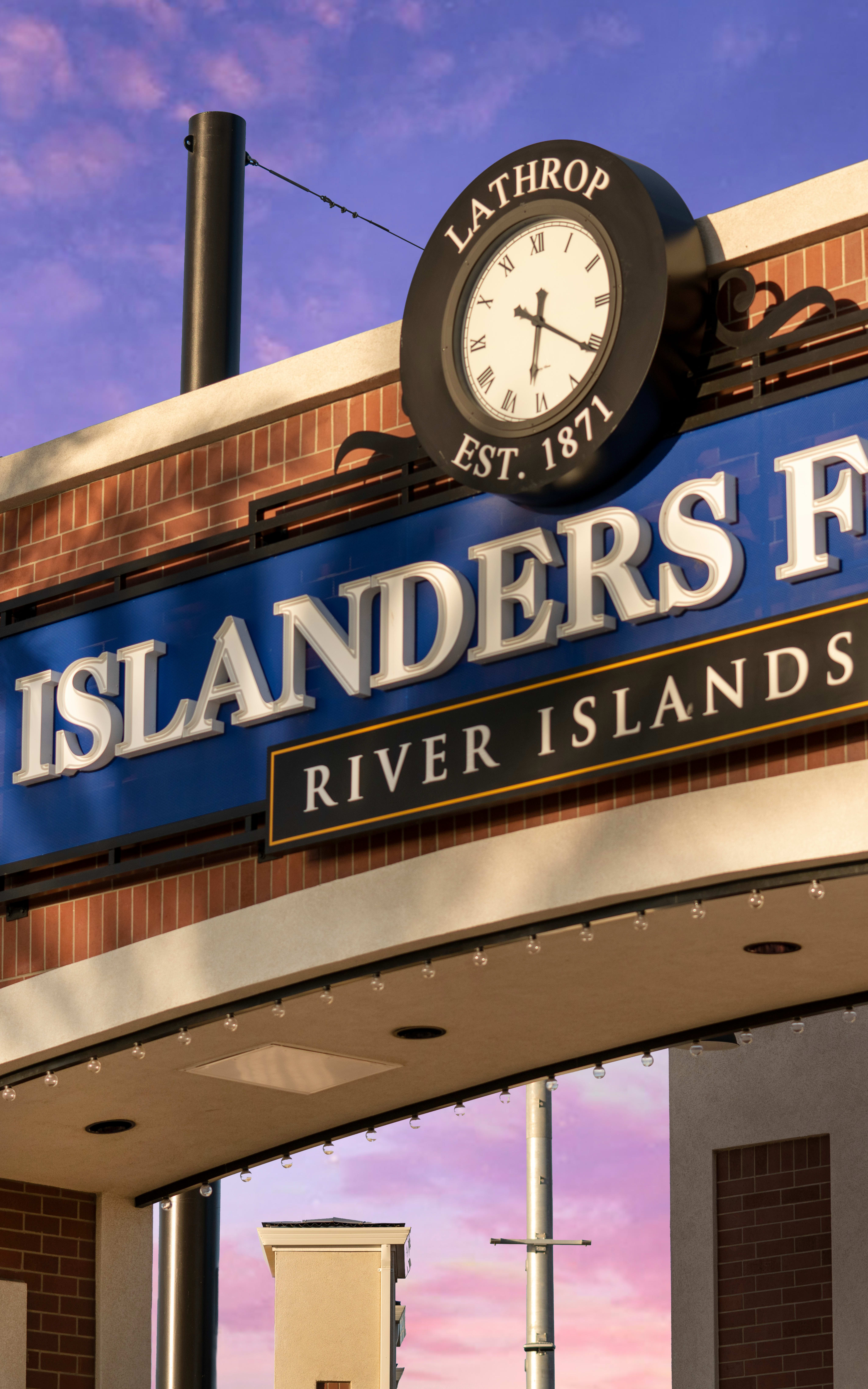 A brick building with a large sign reading "Islanders Field" and a clock tower, set against a vibrant purple and blue sky.