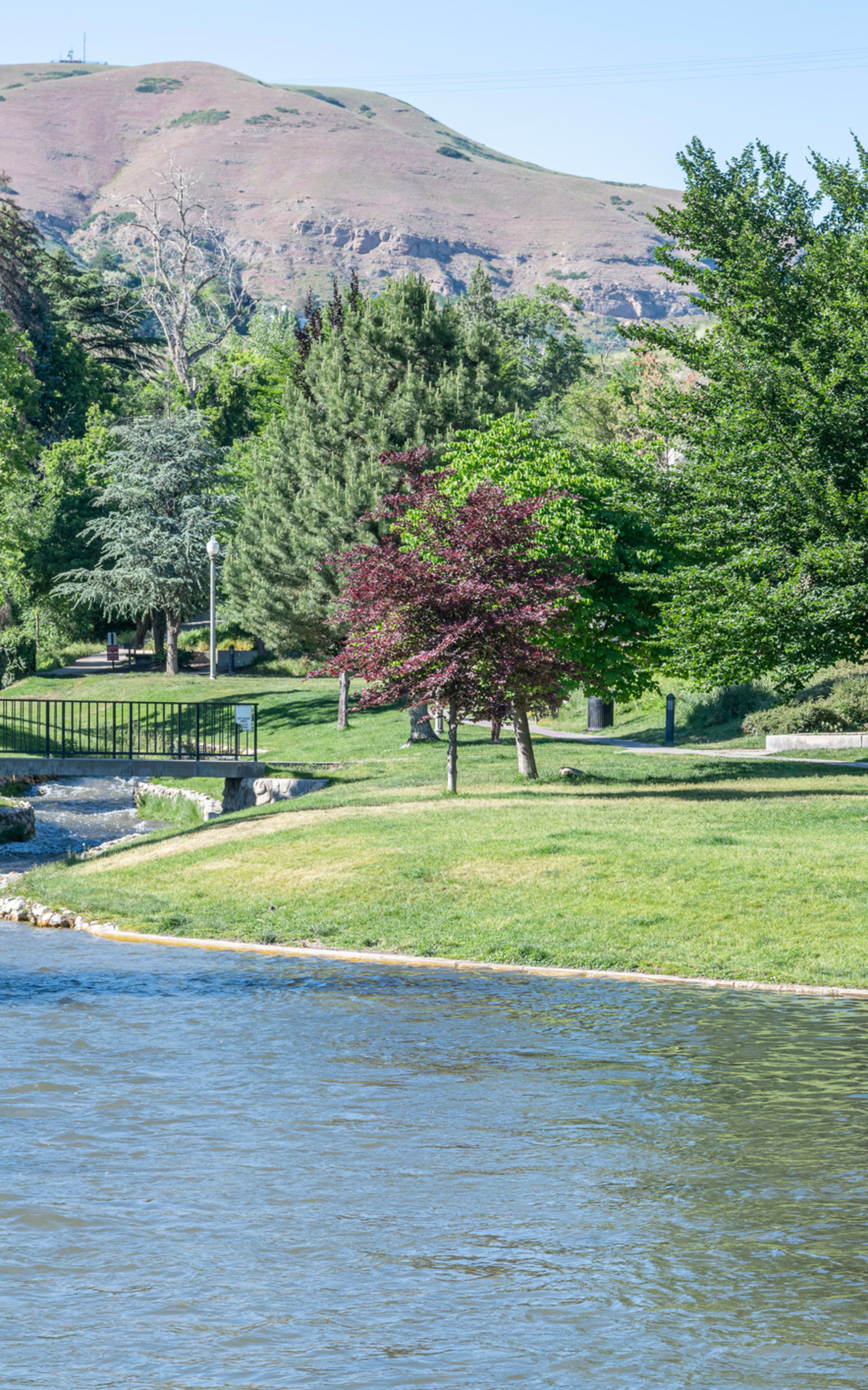 A lush, green park with a winding stream running through it, surrounded by towering mountains in the background.