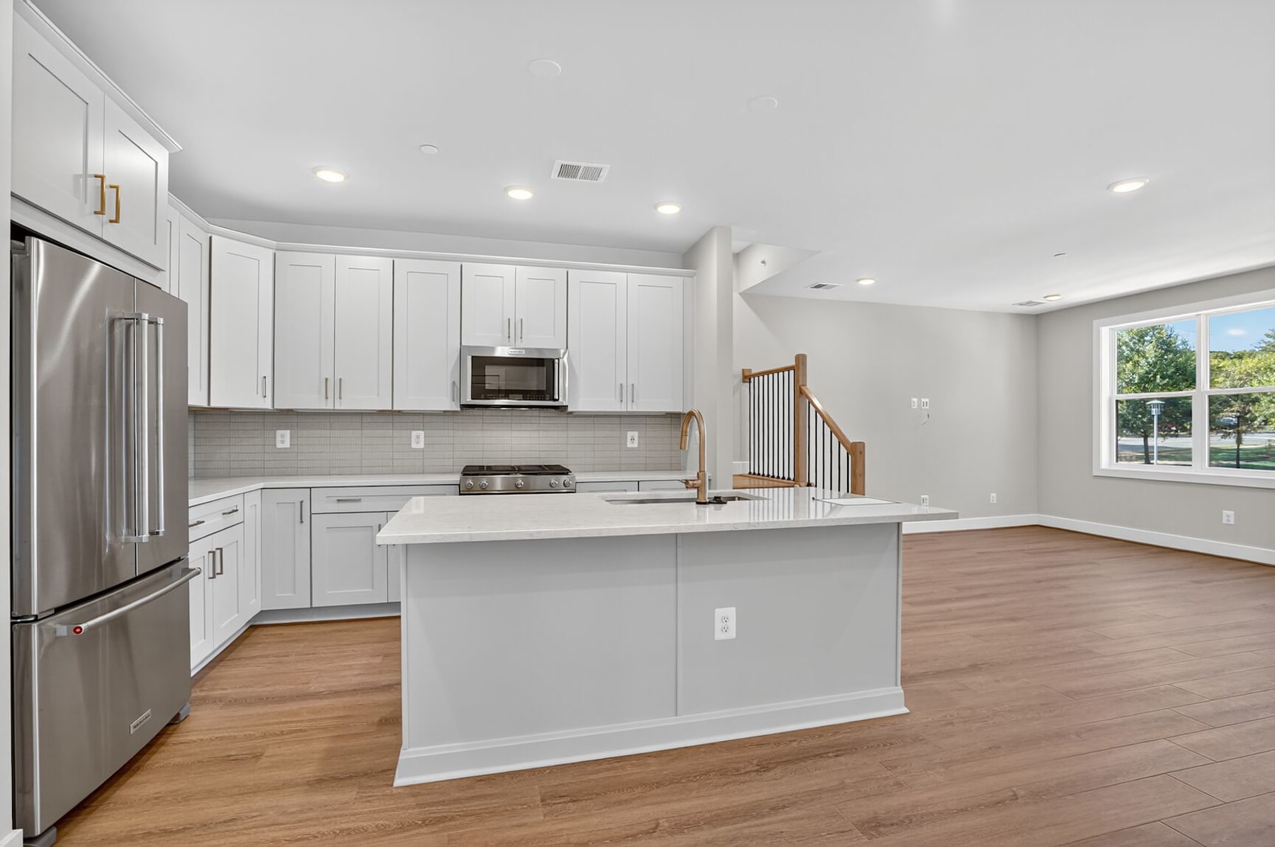 A modern, open-concept kitchen with white cabinets, stainless steel appliances, and a central island with a white countertop, set against a hardwood floor and a bright, airy space.