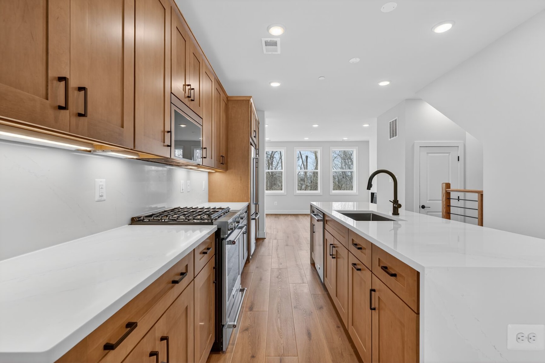 A modern, well-lit kitchen with wooden cabinets, white countertops, and stainless steel appliances, set against a bright and airy background.