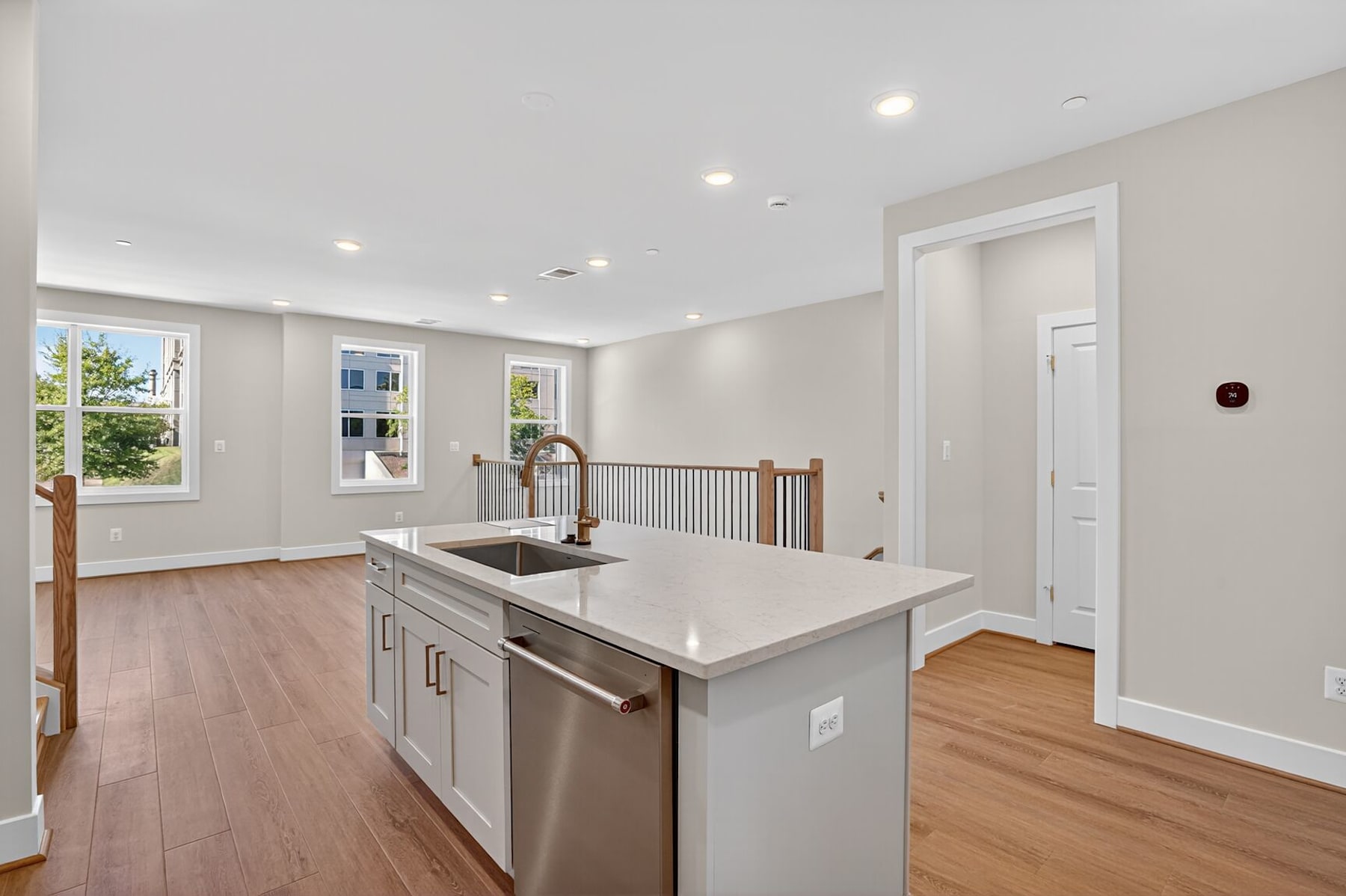 A modern, open-concept kitchen with a large island, stainless steel appliances, and hardwood floors, surrounded by bright windows and a hallway leading to other rooms.