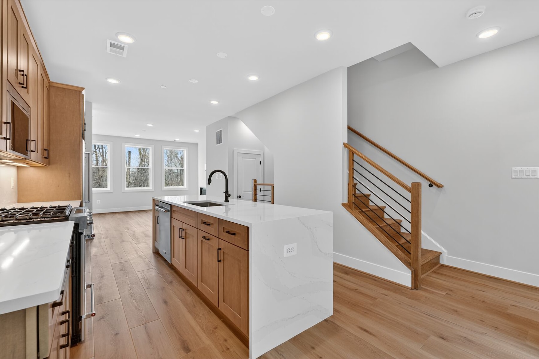 A modern, open-concept kitchen with white countertops, wooden cabinets, and a staircase leading to the upper level in the background.