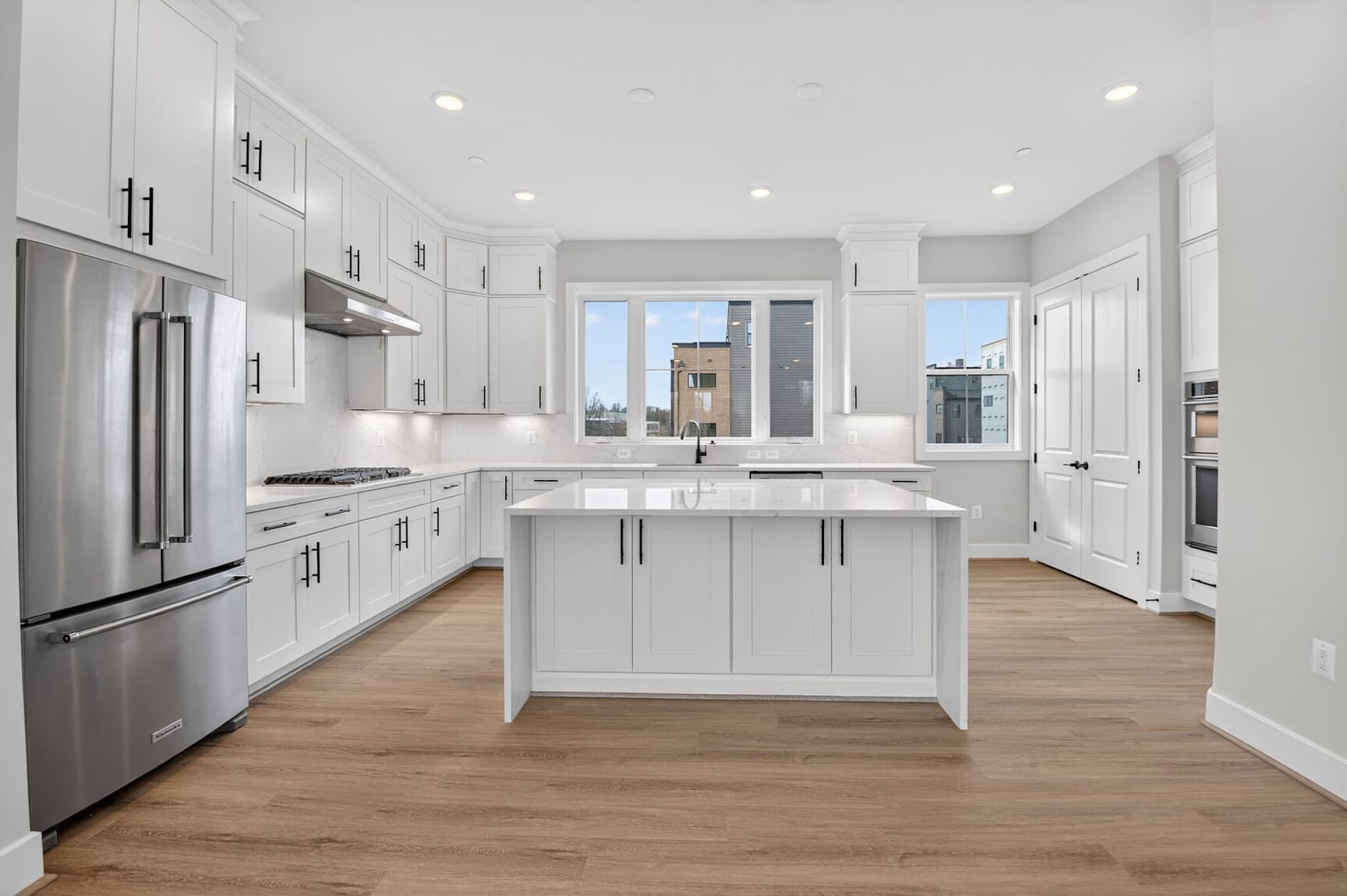 A modern, bright, and spacious kitchen with white cabinets, stainless steel appliances, and a central island with a marble countertop.