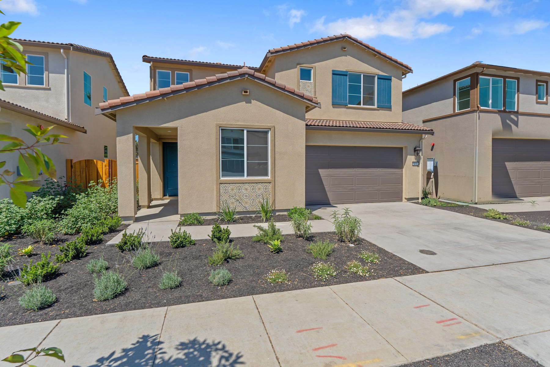 A modern, two-story residential building with a garage, surrounded by landscaped gardens and a paved driveway in the foreground.