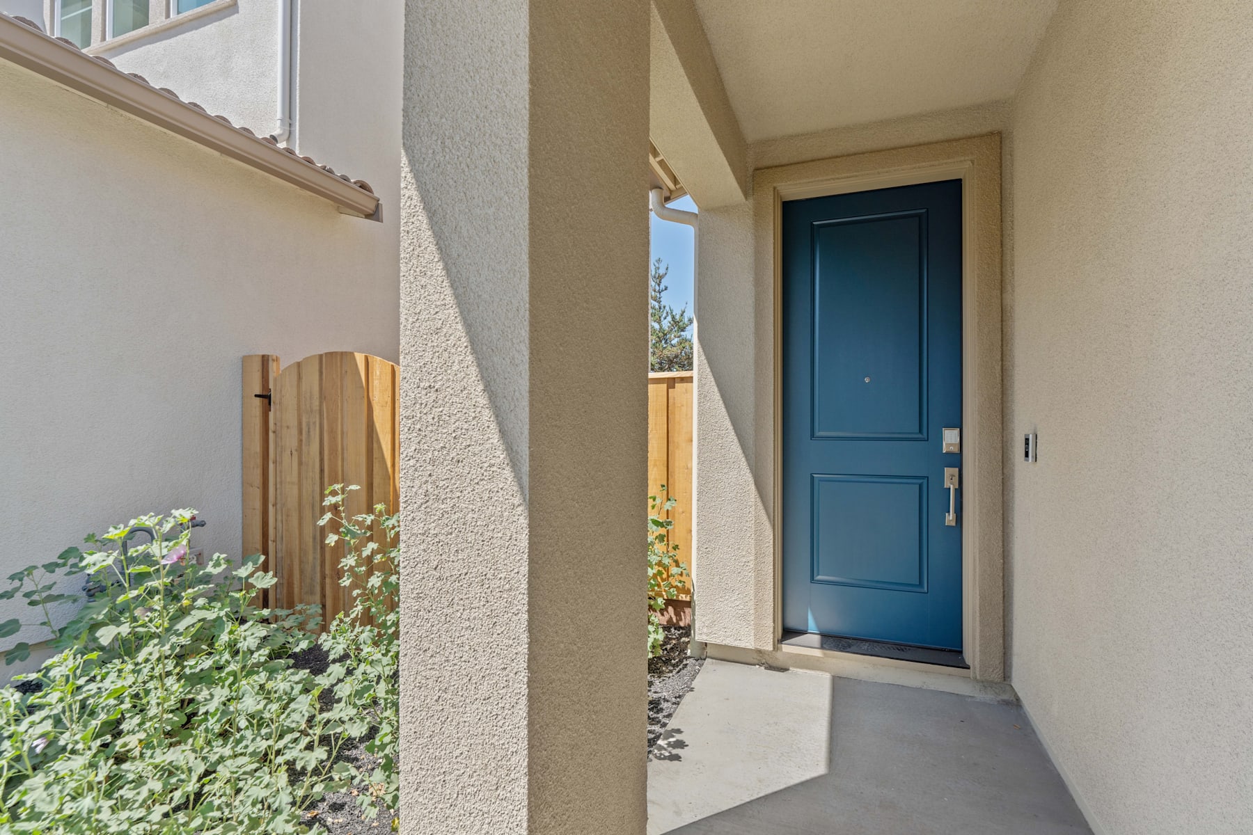 A blue wooden door stands in the foreground, surrounded by a lush garden with greenery and flowers in the background.