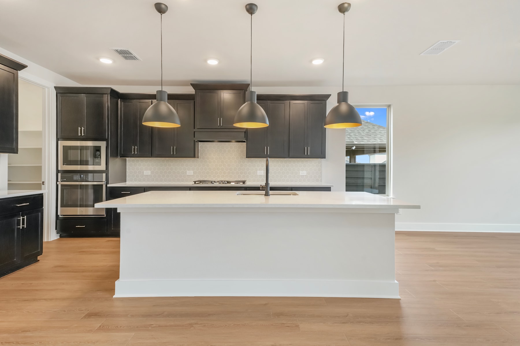 A modern, open-concept kitchen with dark cabinets, a white island, and pendant lights hanging above the counter.