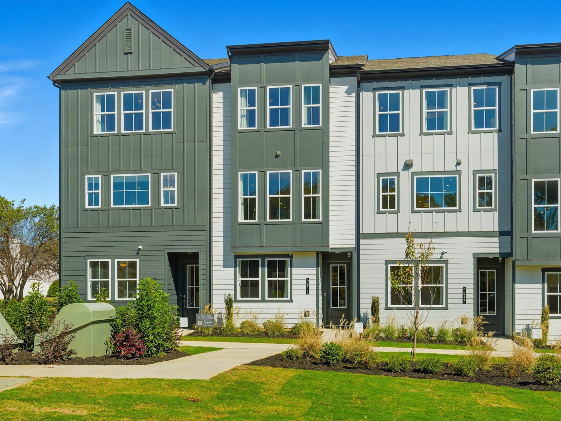 A multi-story residential building with a green exterior, surrounded by a well-manicured lawn and landscaping, stands against a clear blue sky.