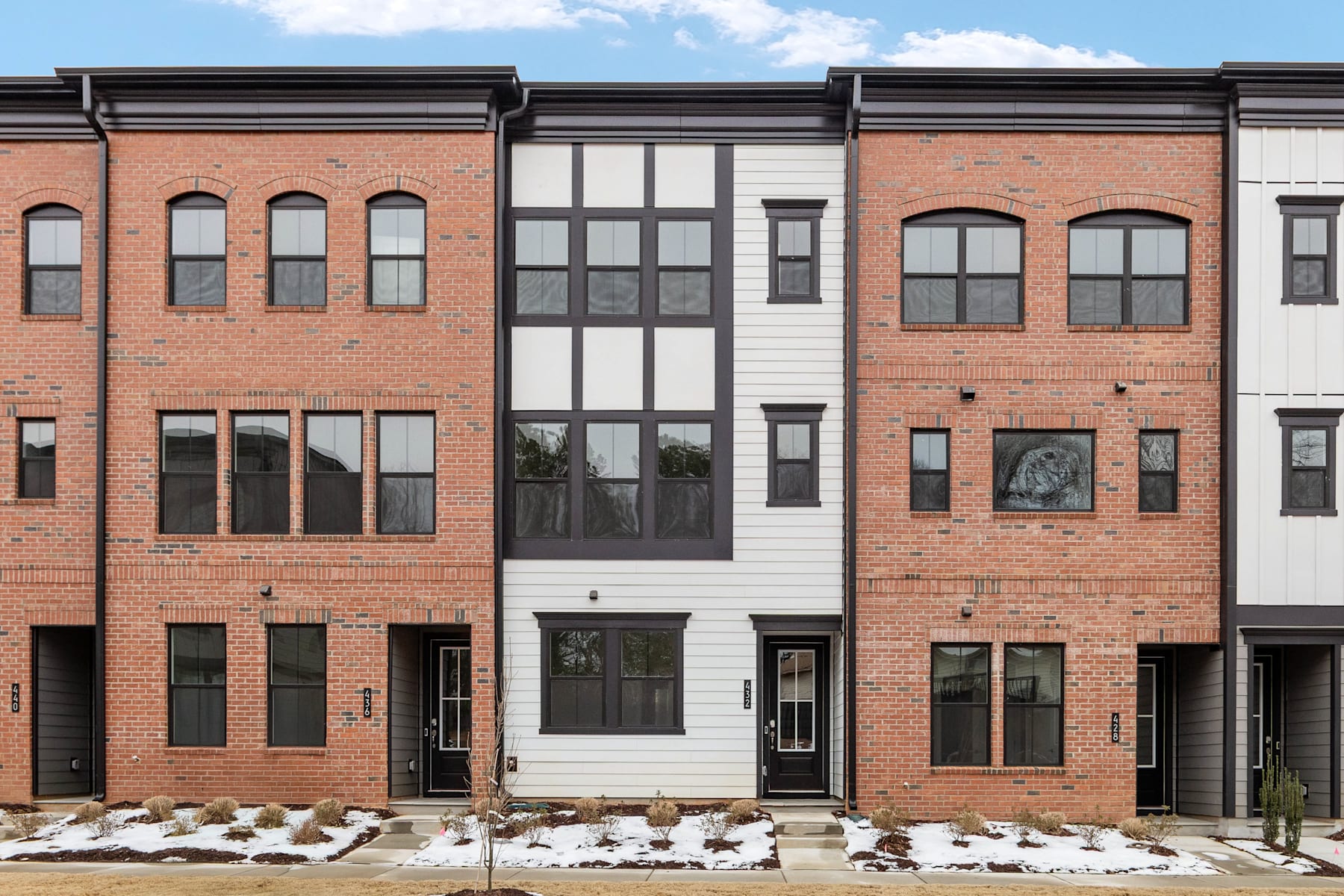 A row of modern, brick townhouses with large windows and a snowy foreground.