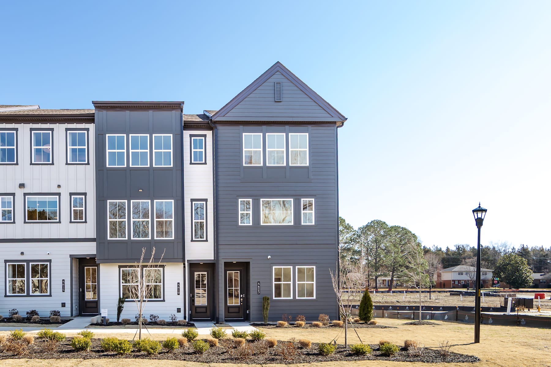 A multi-story townhouse with a gabled roof and large windows, surrounded by landscaped grounds and a lamp post in the foreground.