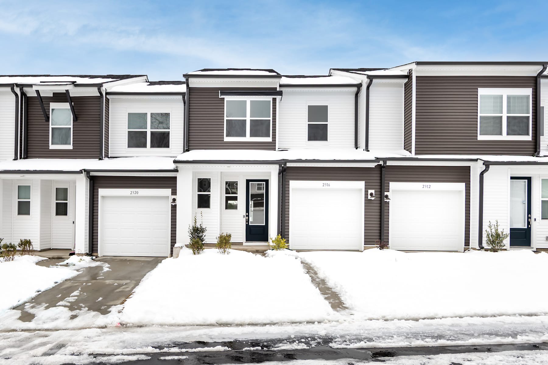 A row of modern townhouses with a snowy foreground, set against a clear blue sky.