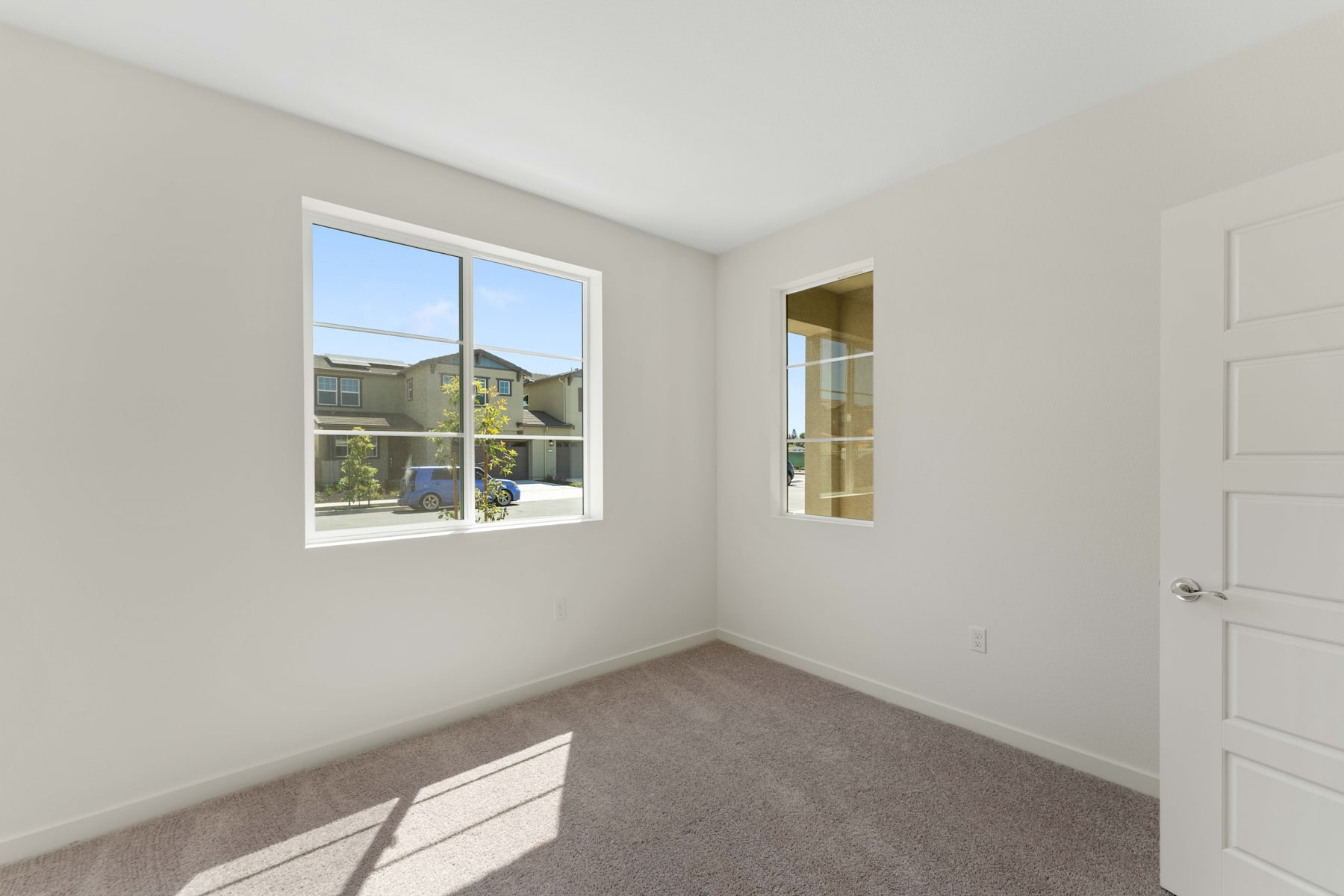 A bright and spacious room with a large window overlooking a grassy outdoor area, and a white door leading to another part of the interior.