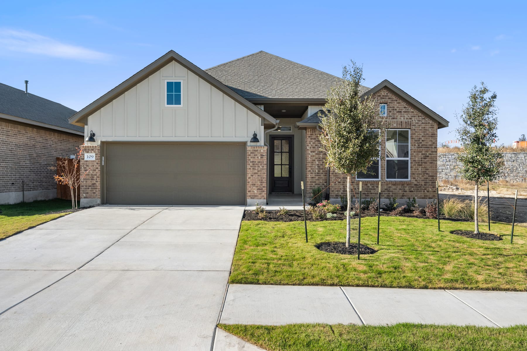 A two-story house with a garage, surrounded by a well-maintained lawn and landscaping, stands against a clear blue sky.