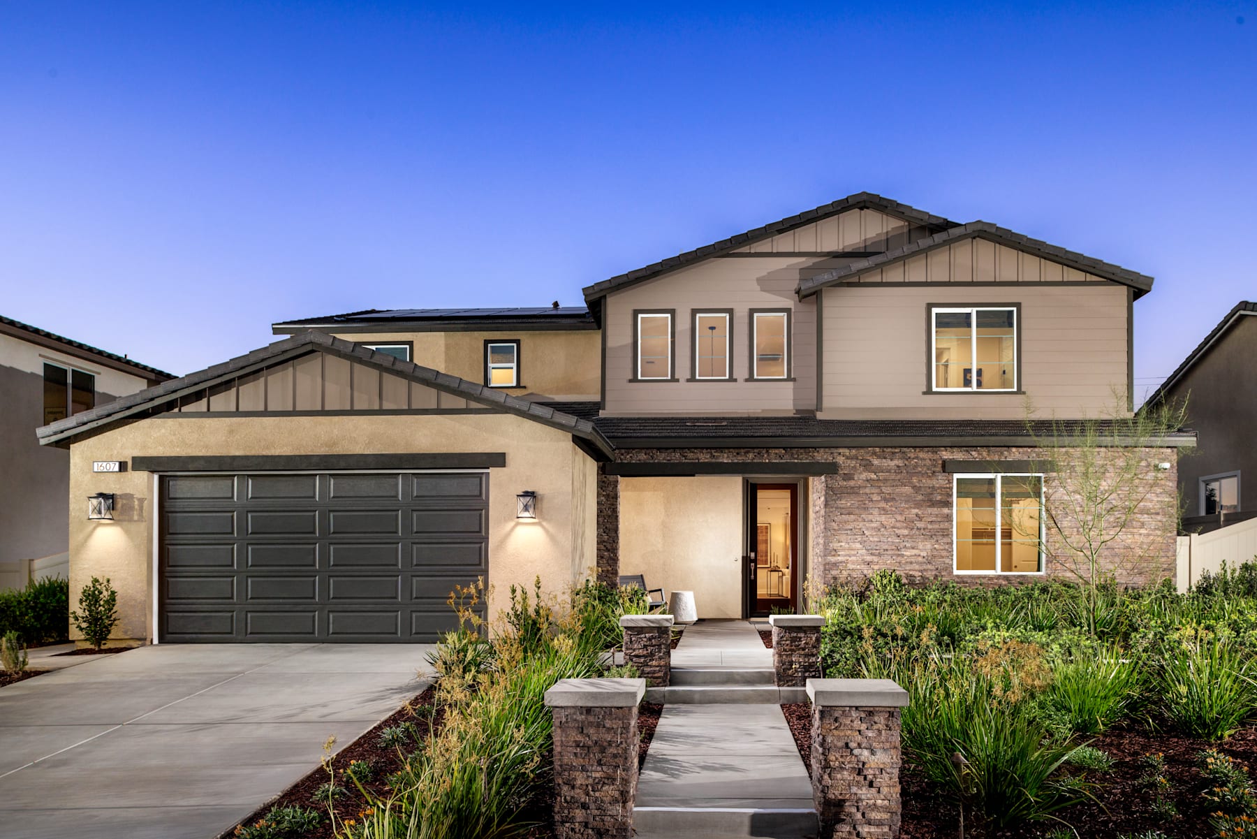 A two-story house with a garage, surrounded by a well-maintained landscaped yard and a clear blue sky in the background.