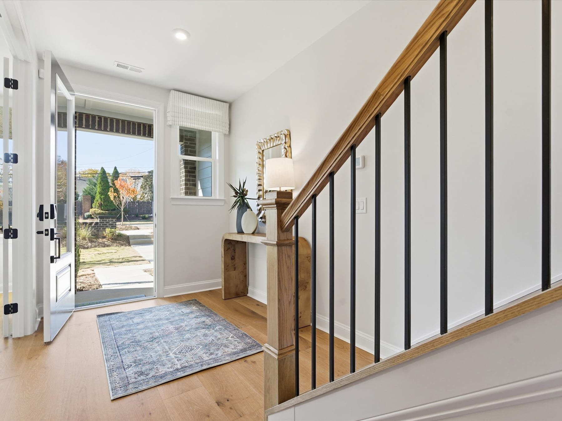 A bright and airy entryway with a wooden staircase, a decorative rug, and a view of the outdoors through the glass door.