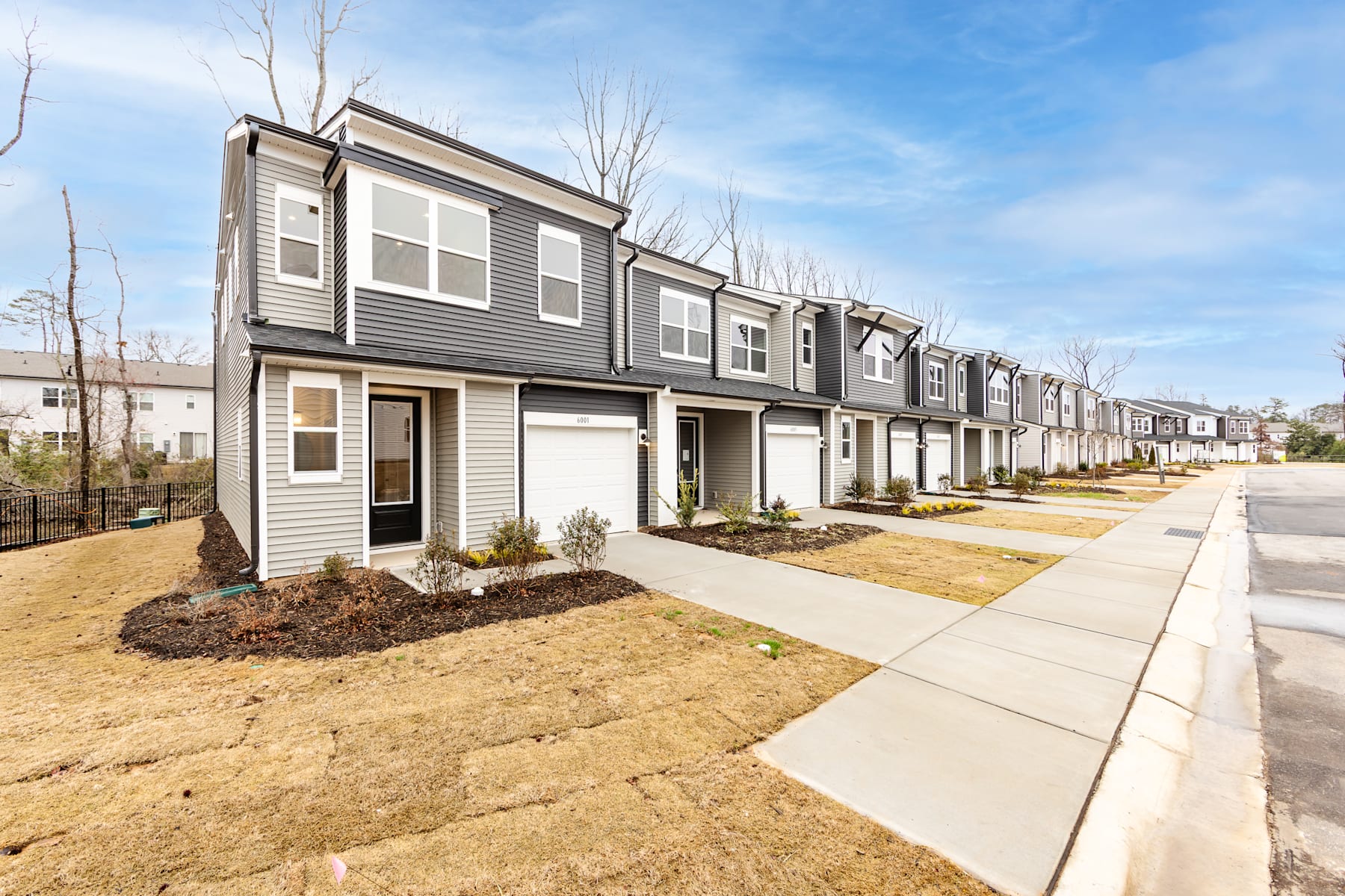 A row of modern, two-story townhouses with gray siding and landscaped yards, set against a backdrop of bare trees and a clear blue sky.