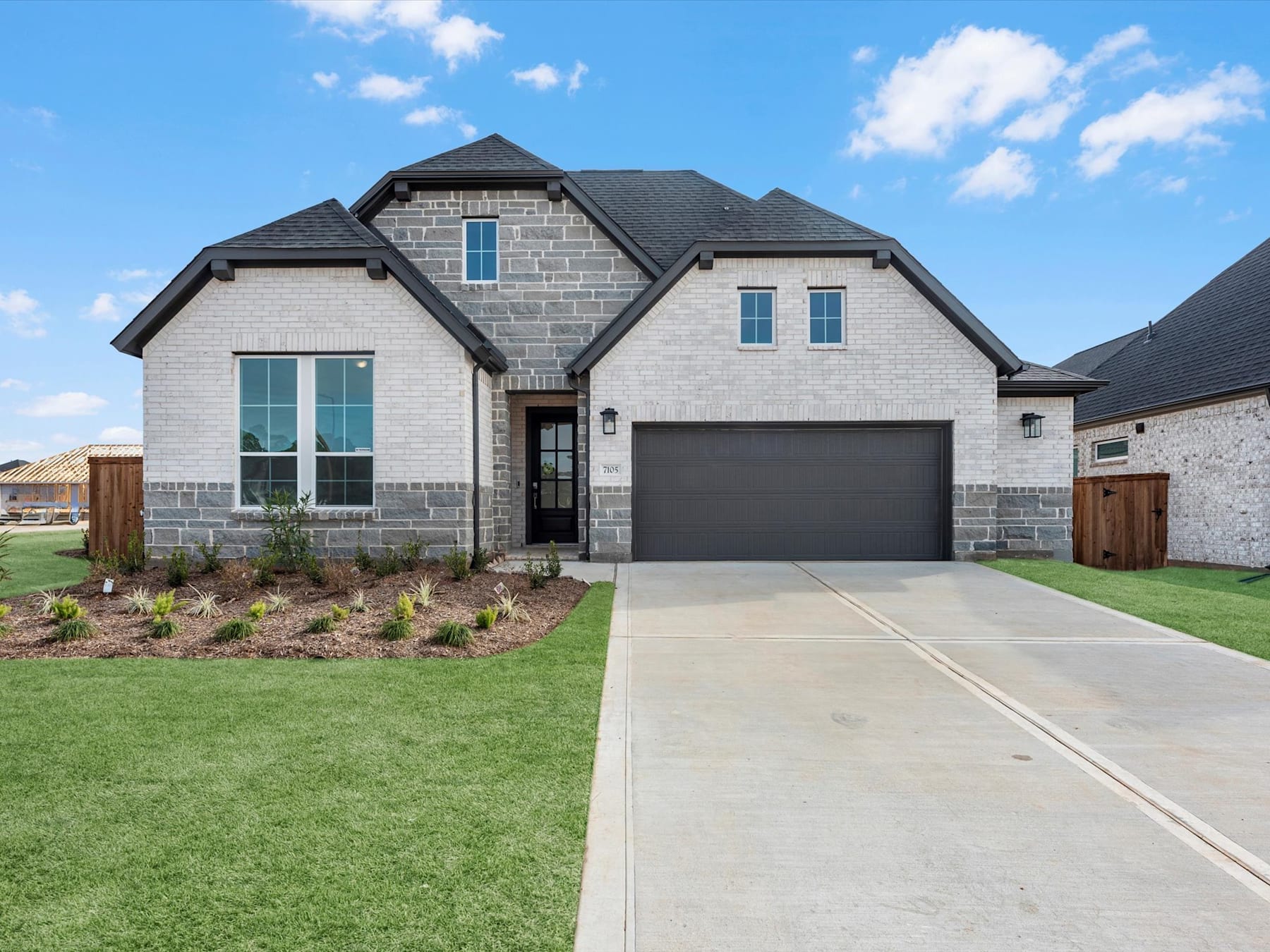 A modern two-story house with a gray exterior, a garage, and a well-manicured lawn in the foreground, set against a clear blue sky with scattered clouds.
