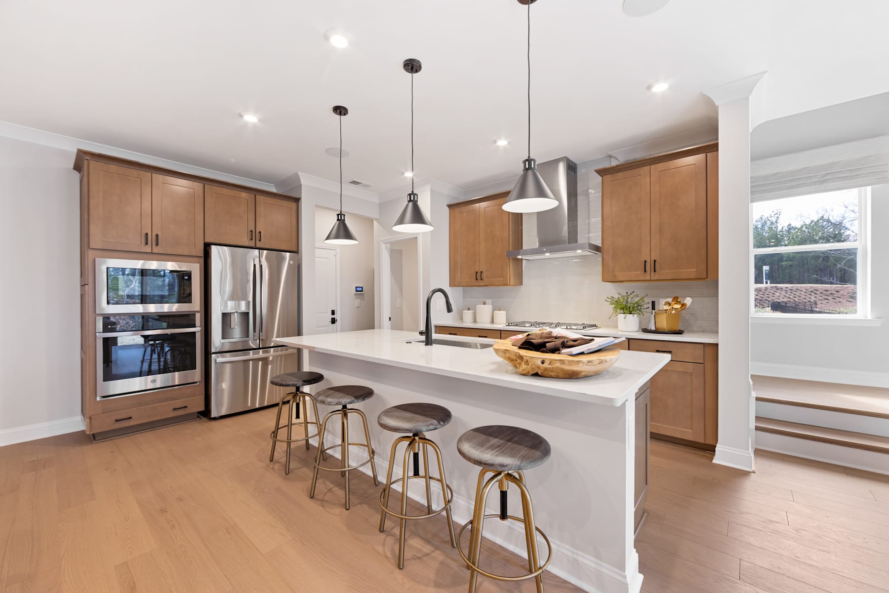 A modern and spacious kitchen with wooden cabinets, a white island, and pendant lights hanging above the counter, creating a warm and inviting atmosphere.