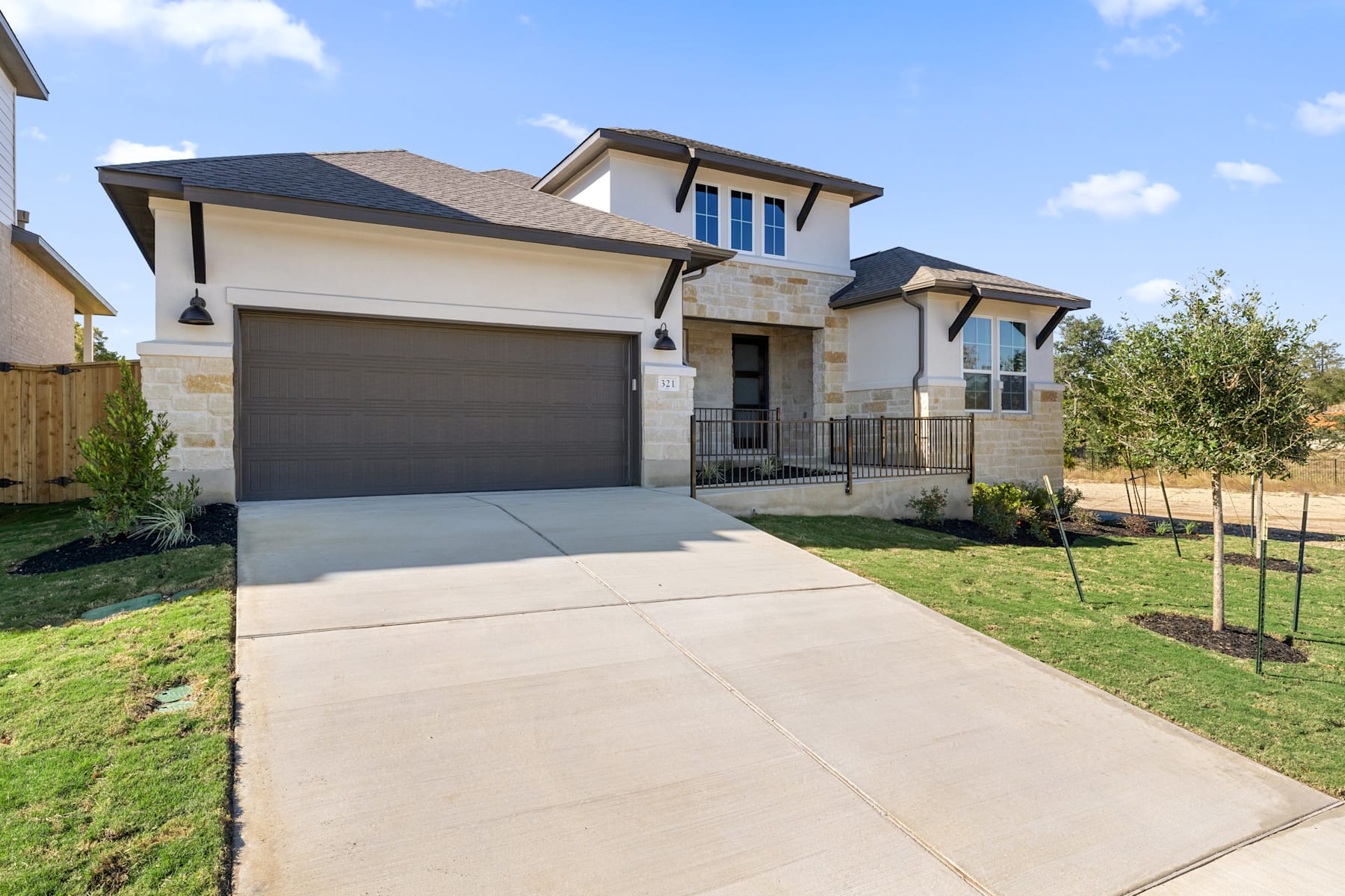 A two-story residential house with a garage, surrounded by a well-maintained lawn and landscaping, set against a blue sky with scattered clouds.