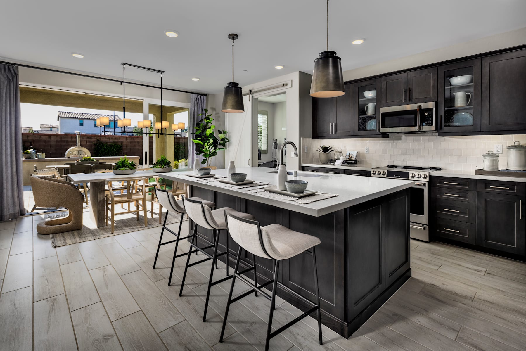 A modern and stylish kitchen with dark cabinets, a large island with bar stools, and a dining area visible in the background.