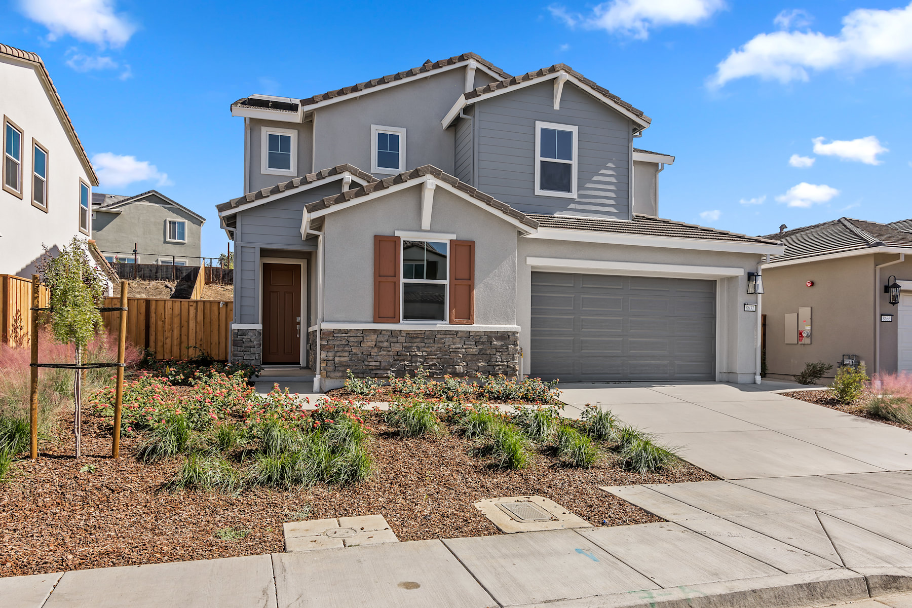 A two-story residential house with a gray exterior, a garage, and a landscaped front yard with a paved walkway leading to the entrance.