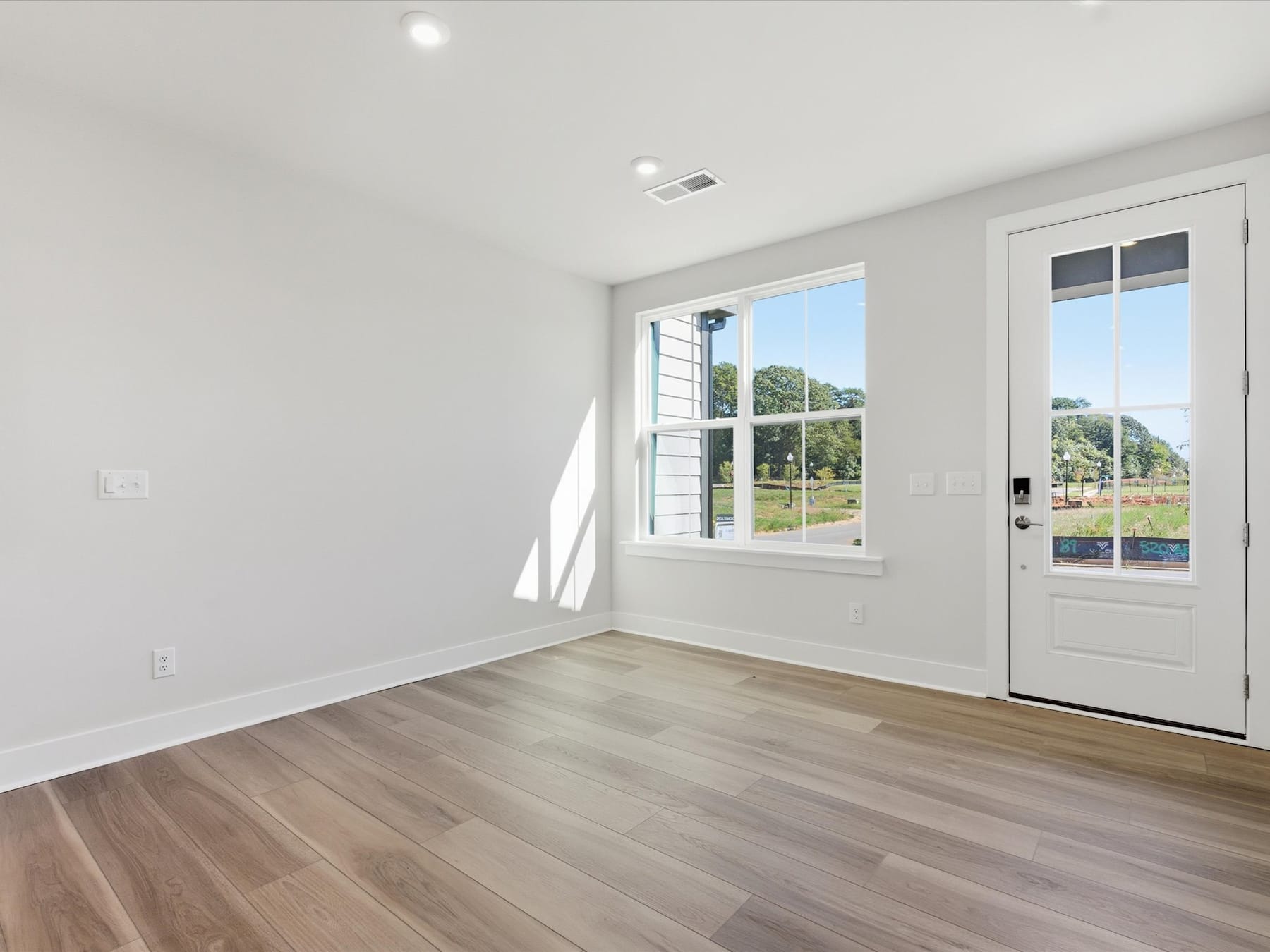 A bright and airy room with large windows overlooking a scenic outdoor landscape, featuring hardwood floors and a glass door leading to the exterior.