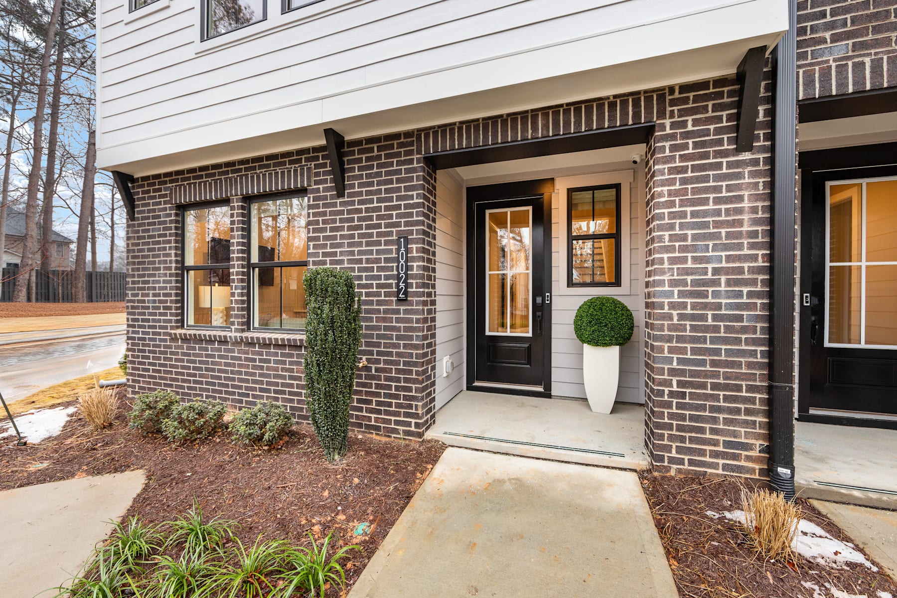 A modern two-story brick house with a covered entryway, surrounded by landscaping and a concrete walkway leading to the front door.