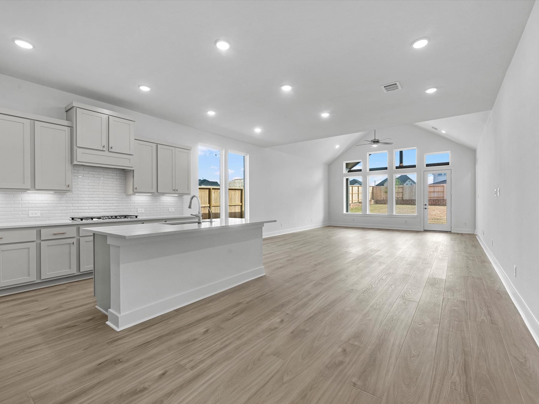 A spacious, modern kitchen with white cabinets, a large island, and hardwood floors, surrounded by large windows that let in ample natural light.