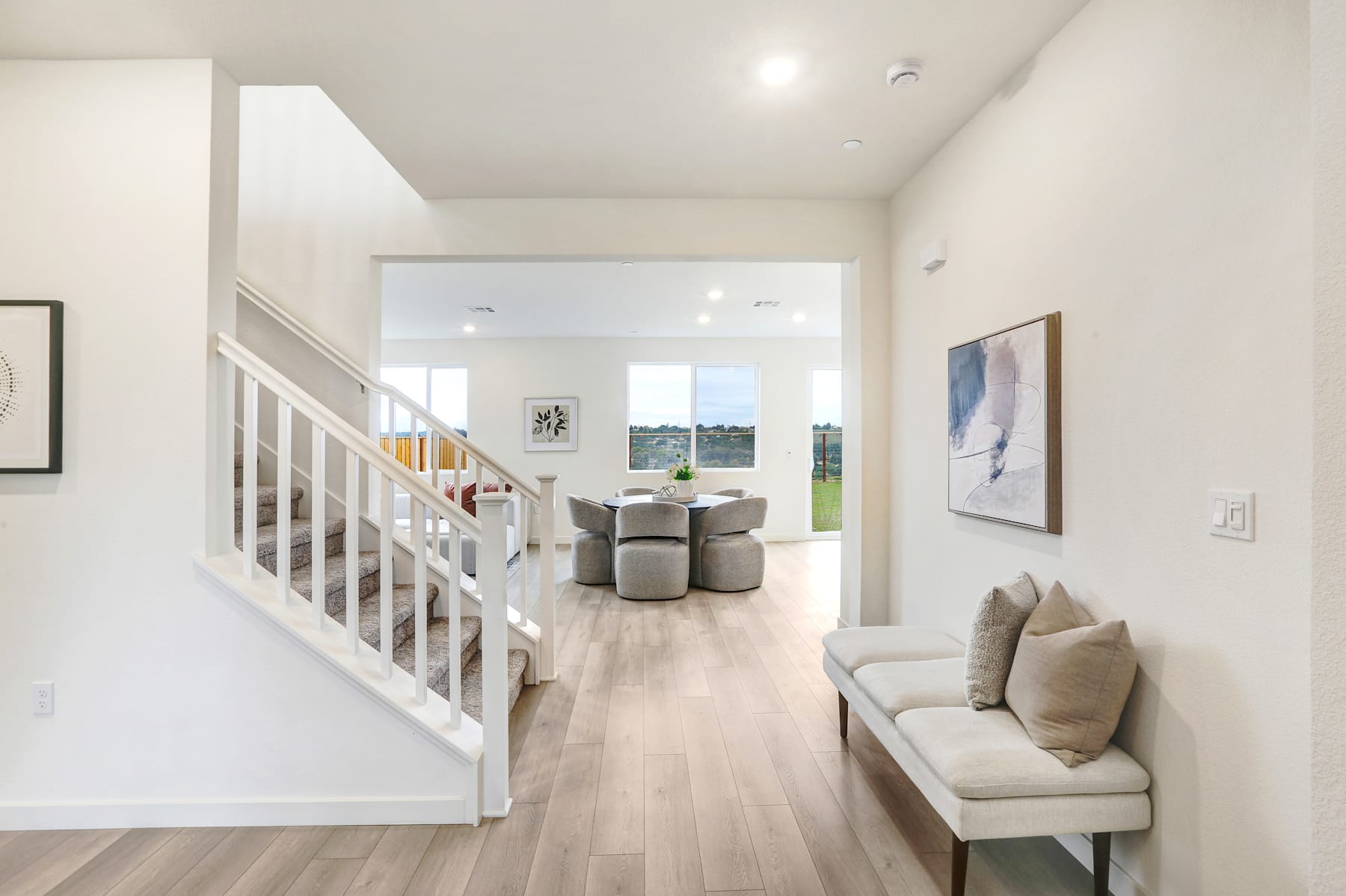 A bright and airy interior with a staircase leading to an open living area, featuring a couch and artwork on the walls.