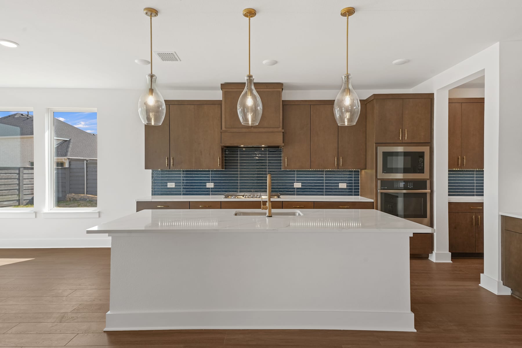 A modern and spacious kitchen with a white island, wooden cabinets, and pendant lights hanging above the counter.