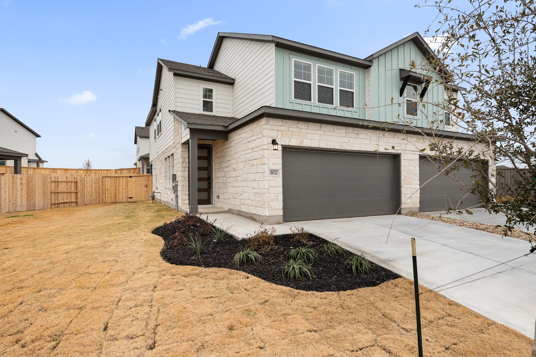 A two-story residential house with a garage, surrounded by a landscaped yard and a wooden fence in the foreground.
