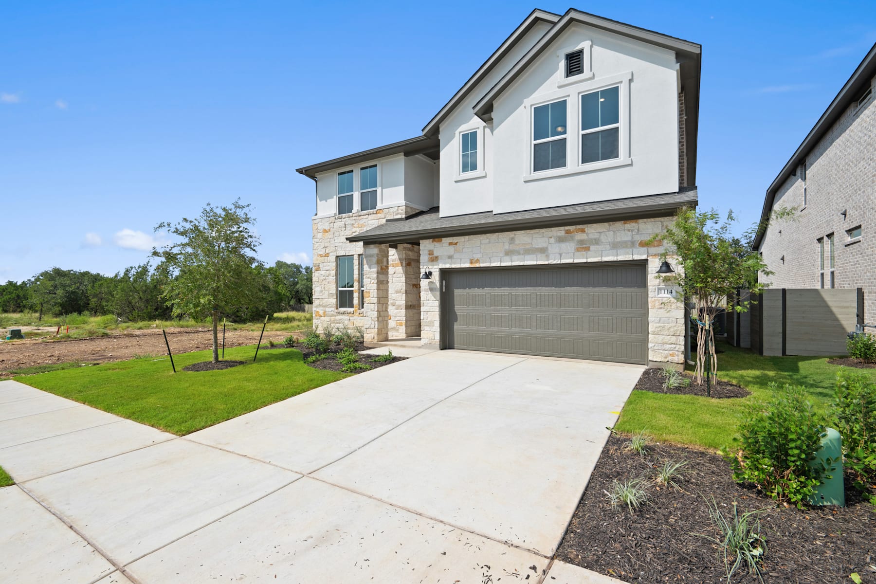 A modern two-story house with a gray exterior, a garage, and a well-manicured lawn surrounded by trees in a residential neighborhood.