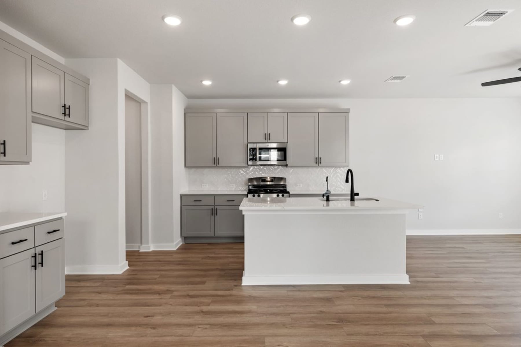 A modern, open-concept kitchen with gray cabinets, a white island, and hardwood floors.
