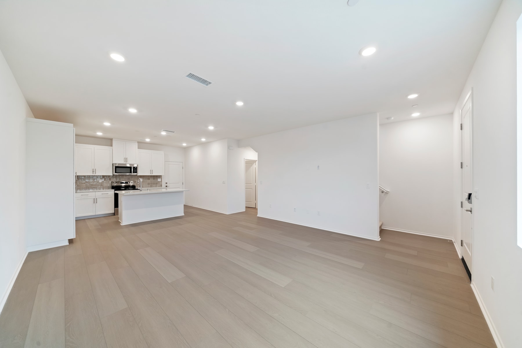 A spacious, open-concept living area with a modern kitchen, hardwood floors, and recessed lighting, creating a bright and airy atmosphere.