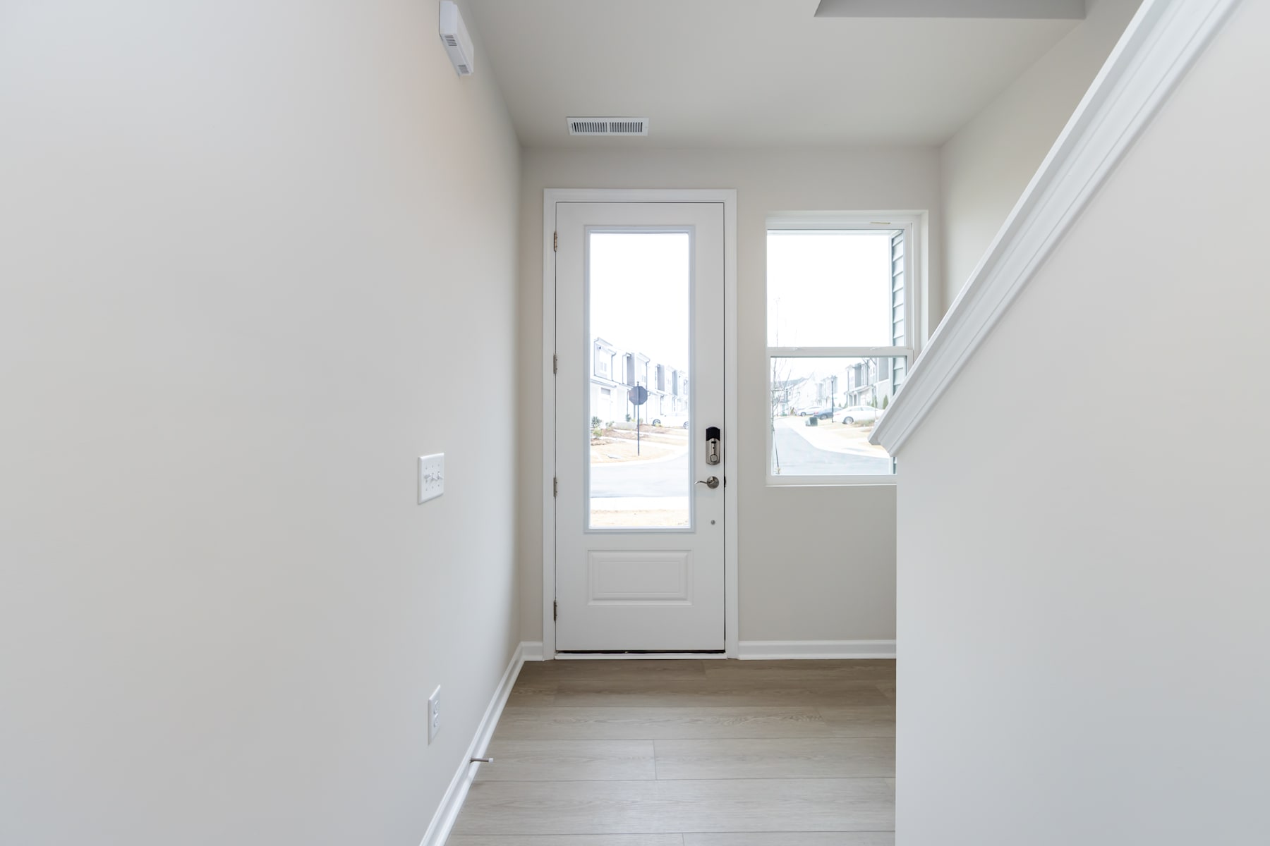 A bright, minimalist entryway with a white door and windows, leading to a hallway with light-colored flooring.