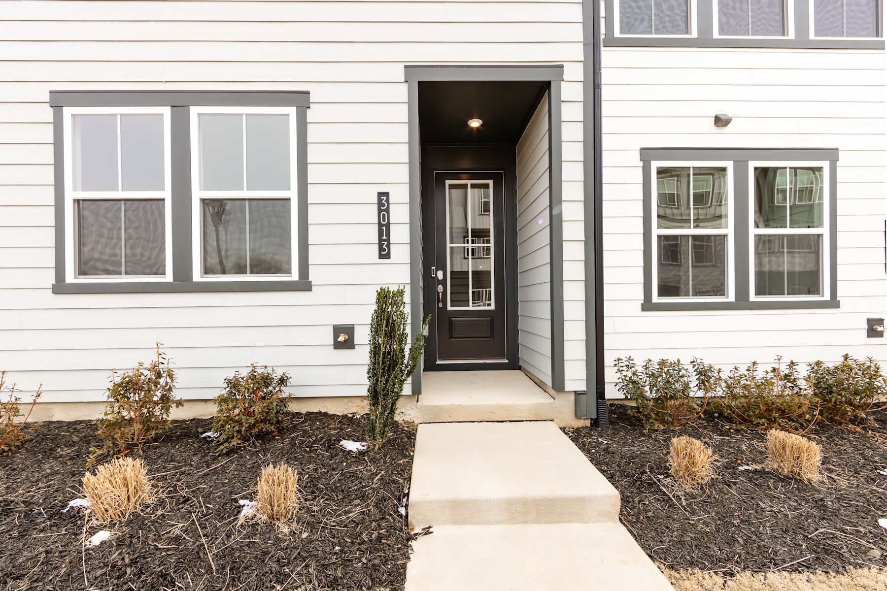 A modern, two-story residential building with a paved walkway leading to the front entrance, surrounded by landscaped vegetation.