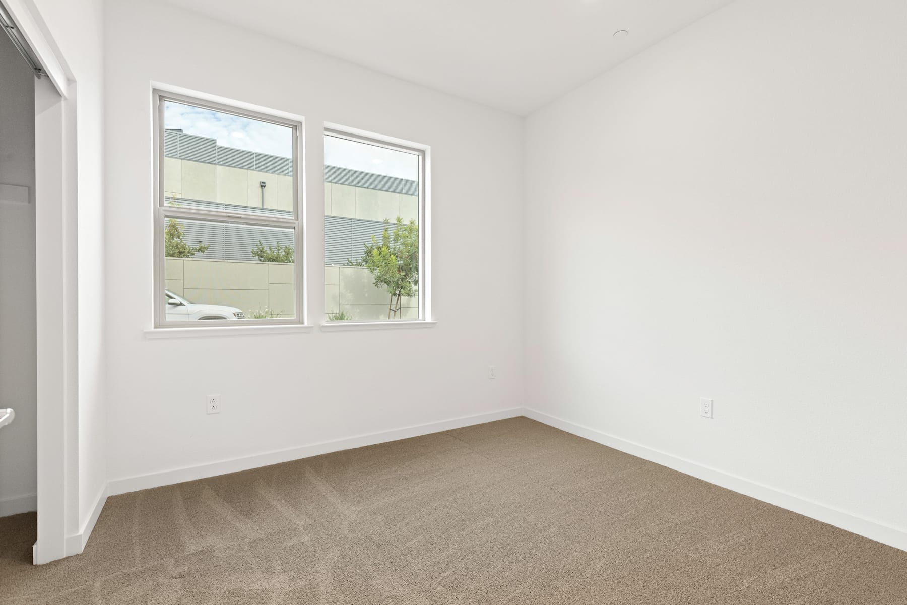 A bright, minimalist room with large windows overlooking a greenery-filled outdoor space.