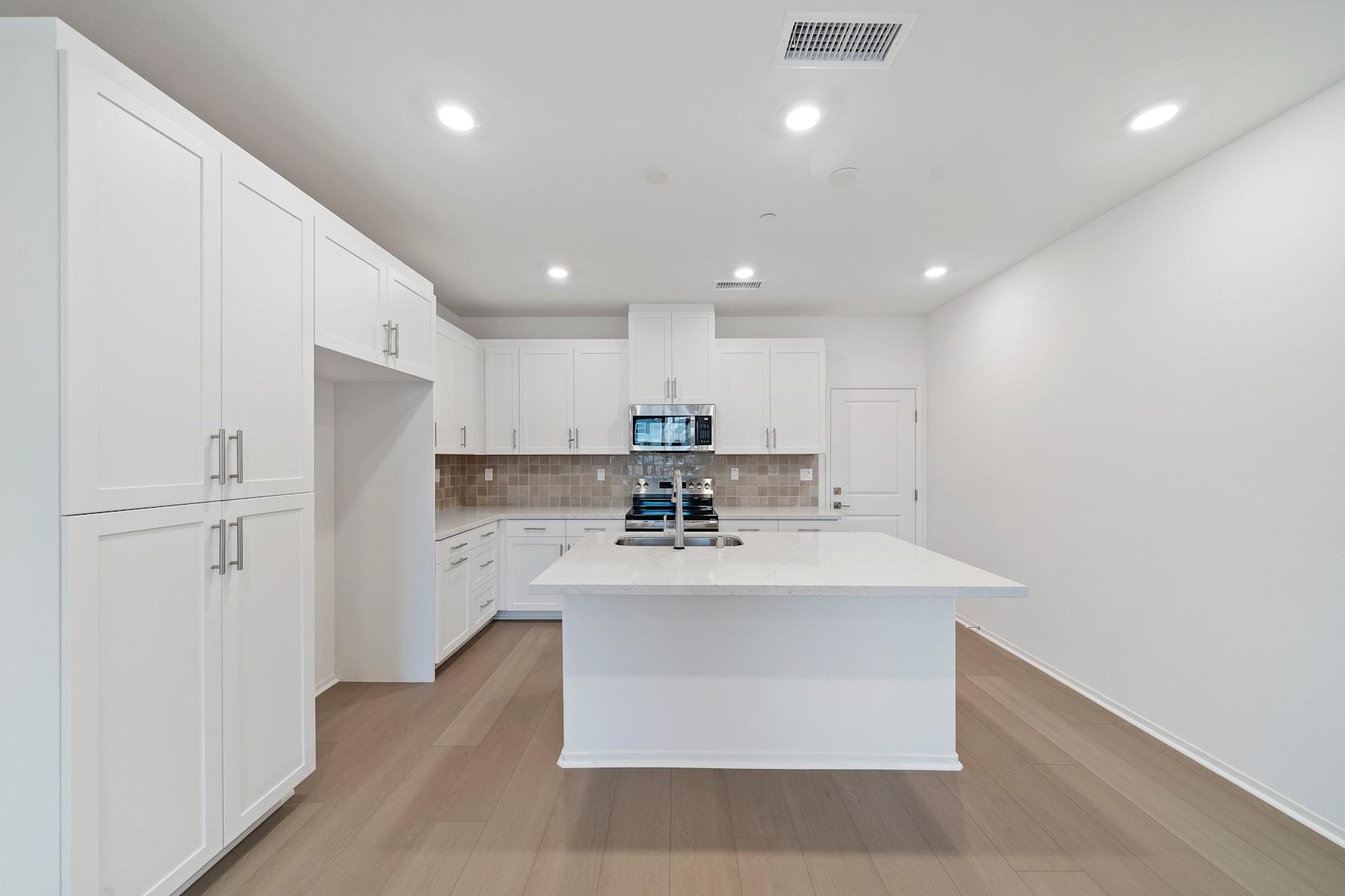 A modern, minimalist kitchen with white cabinets, a large white island, and hardwood floors.
