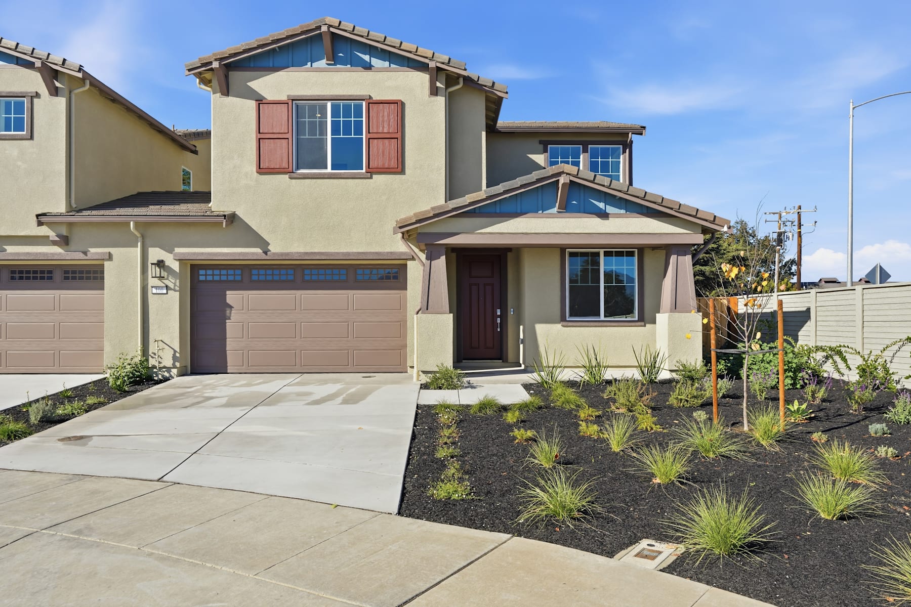A two-story residential house with a landscaped front yard, featuring a paved driveway and a well-maintained garden with various plants and shrubs.