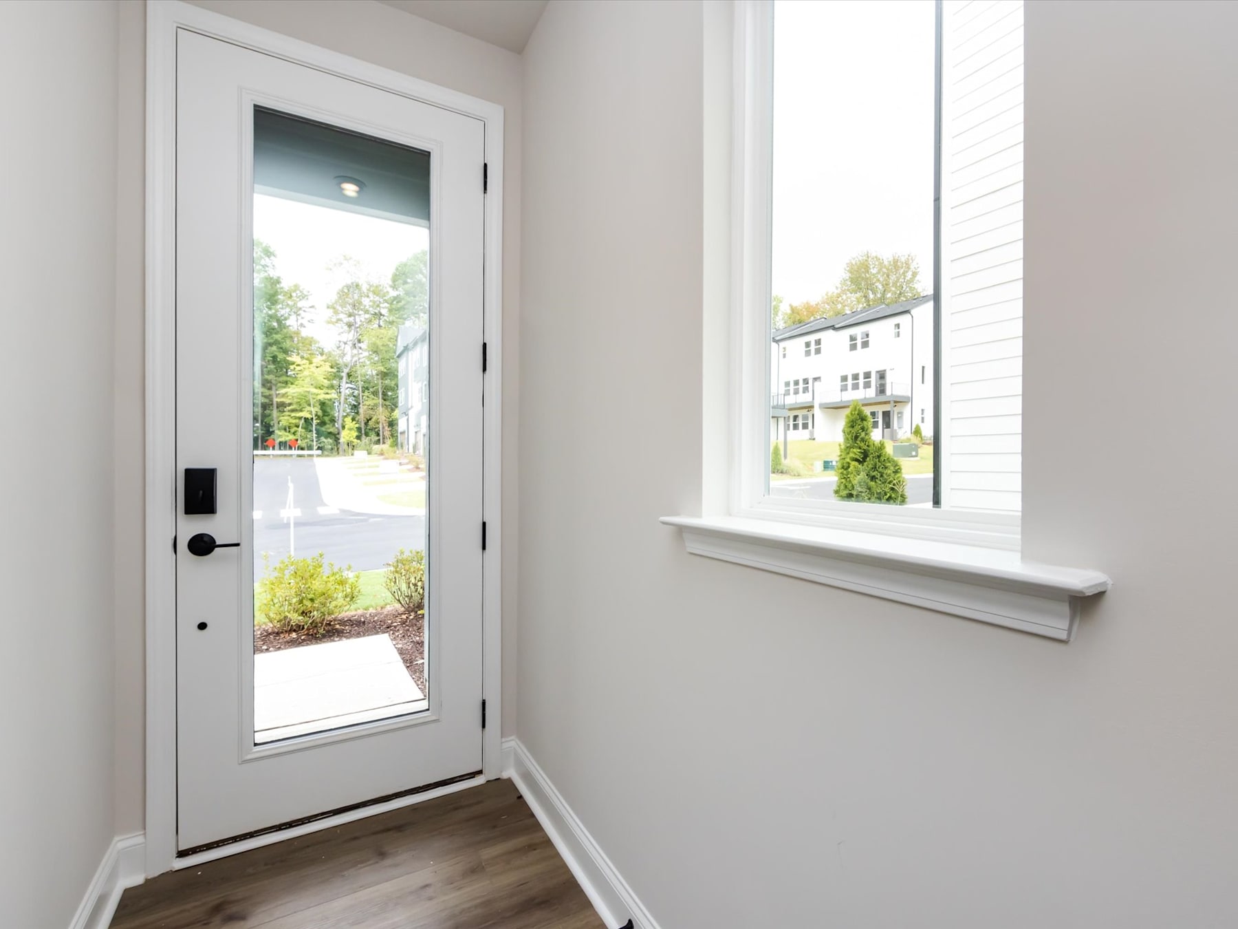 A bright and airy entryway with a white door leading to a lush, green outdoor scene, and a large window providing natural light and a view of the surrounding landscape.