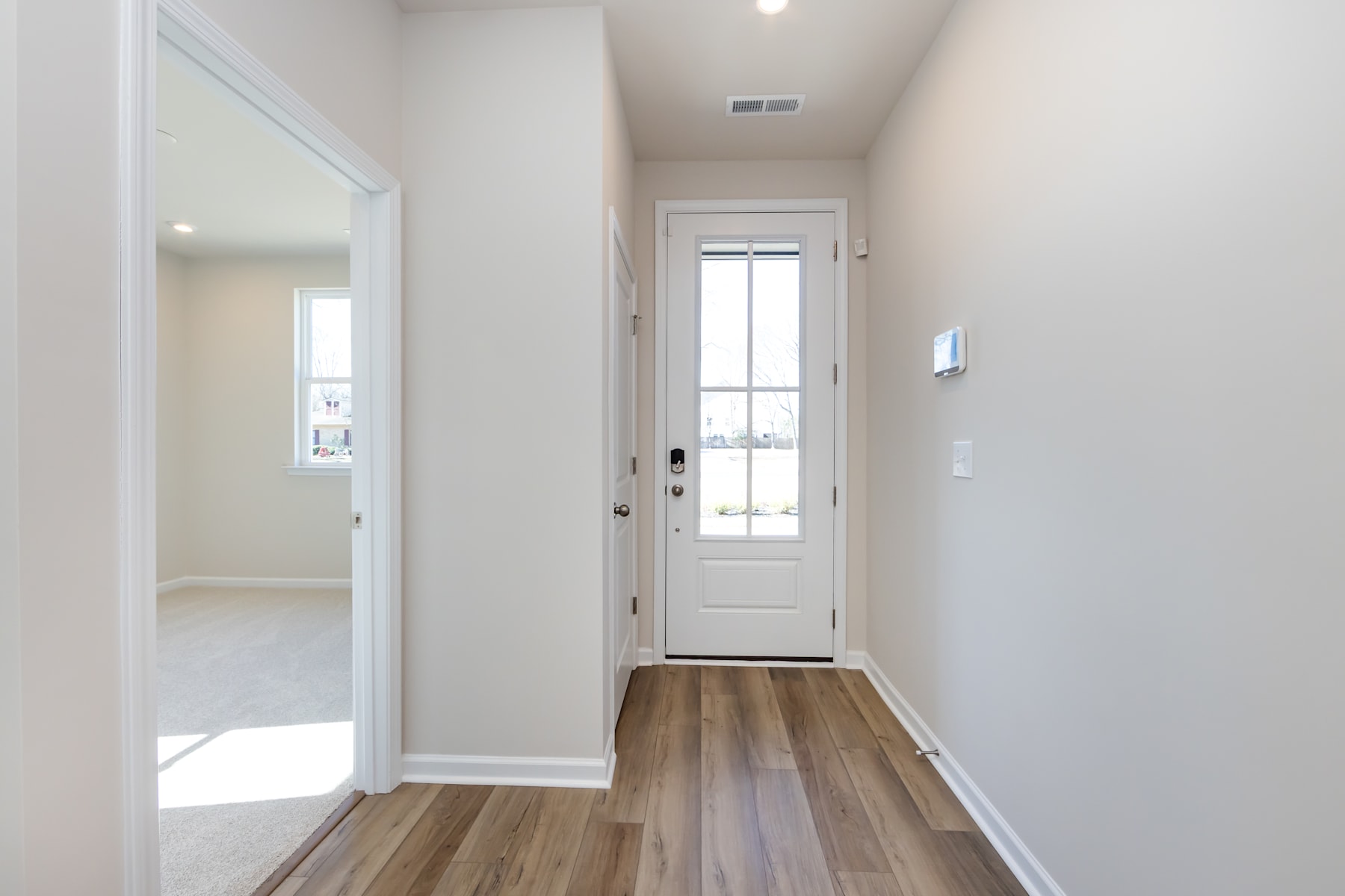 A bright and spacious hallway with a white door leading to the exterior and a wooden floor running through the space.