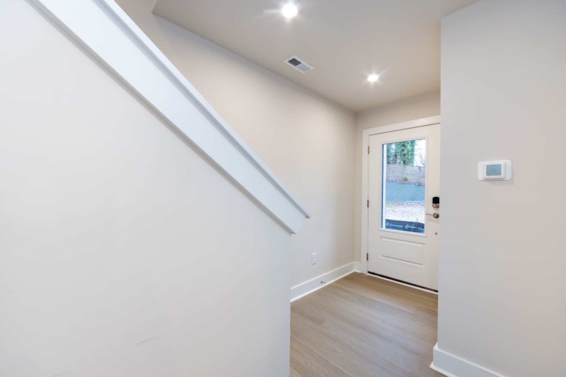 A bright and spacious entryway with a white door leading to the outdoors, hardwood flooring, and recessed lighting fixtures on the ceiling.