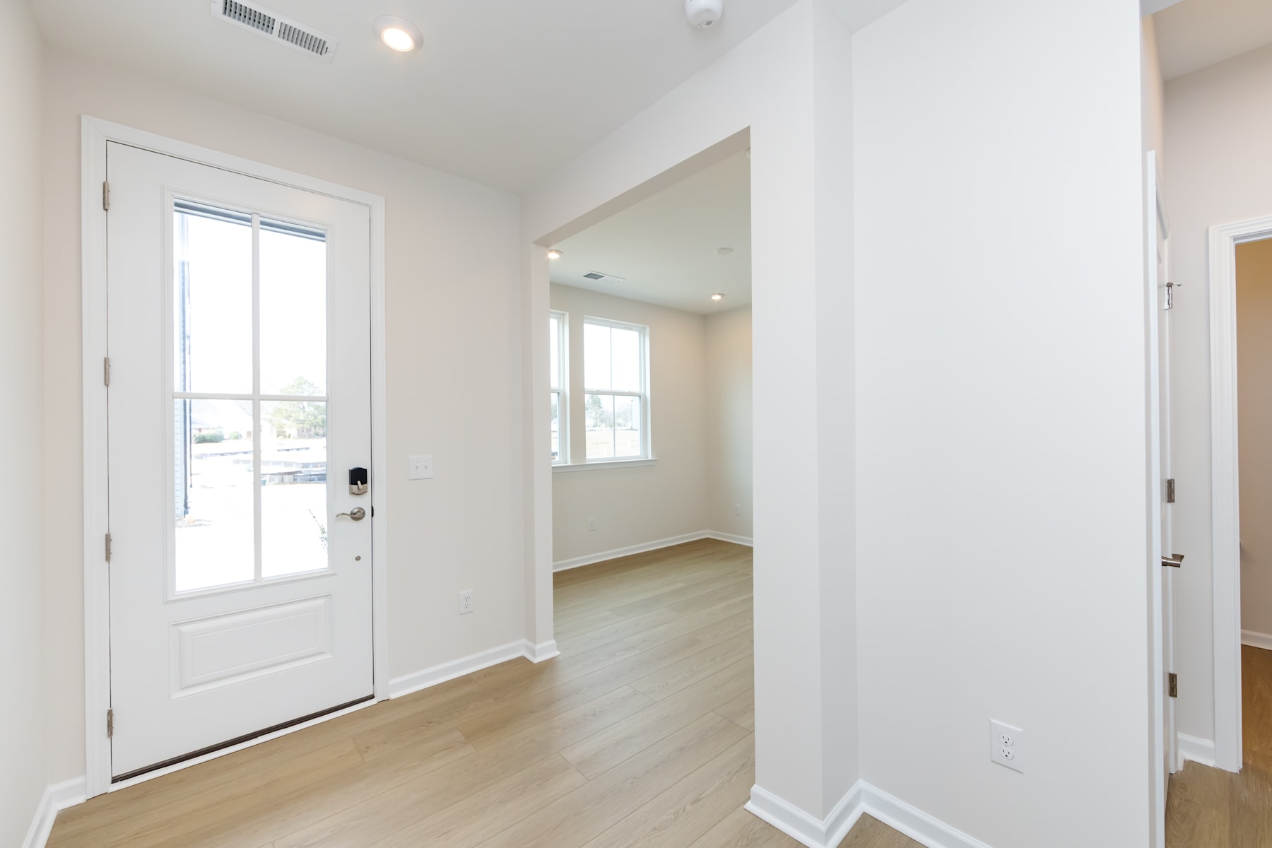A bright and spacious entryway with a white front door, hardwood floors, and a hallway leading to other rooms.