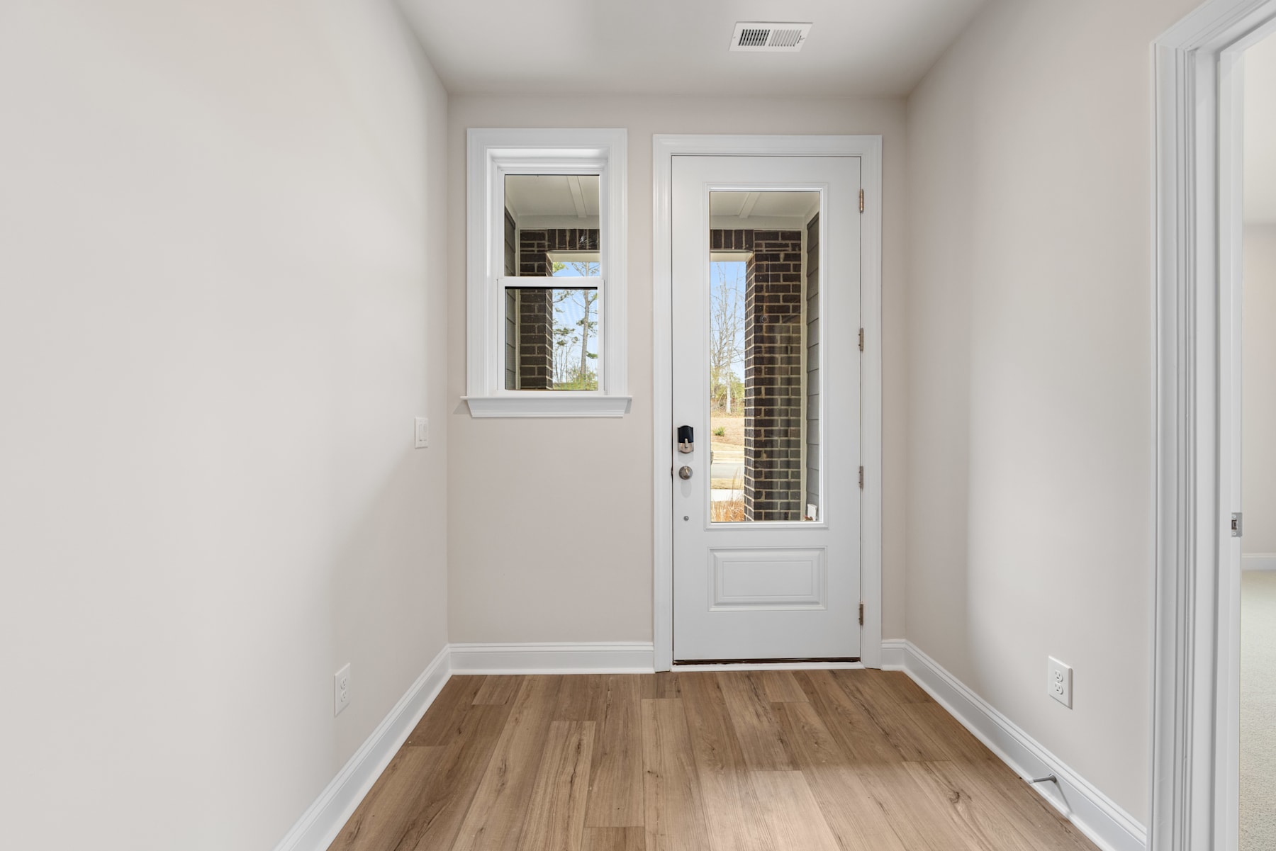A bright and airy hallway with a white door leading to the exterior, featuring hardwood floors and a minimalist design.