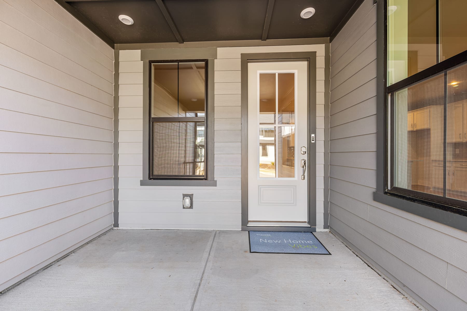 A modern, minimalist entryway with a white wooden exterior, a glass door, and a welcome mat on the concrete floor.