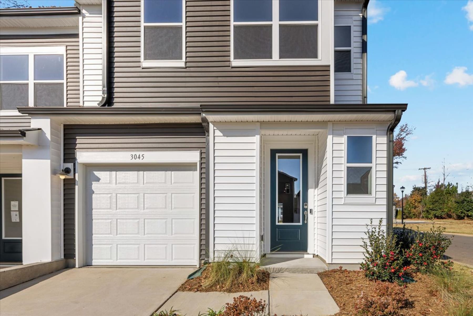 A two-story residential building with a white garage door, a blue front door, and landscaping in the foreground.